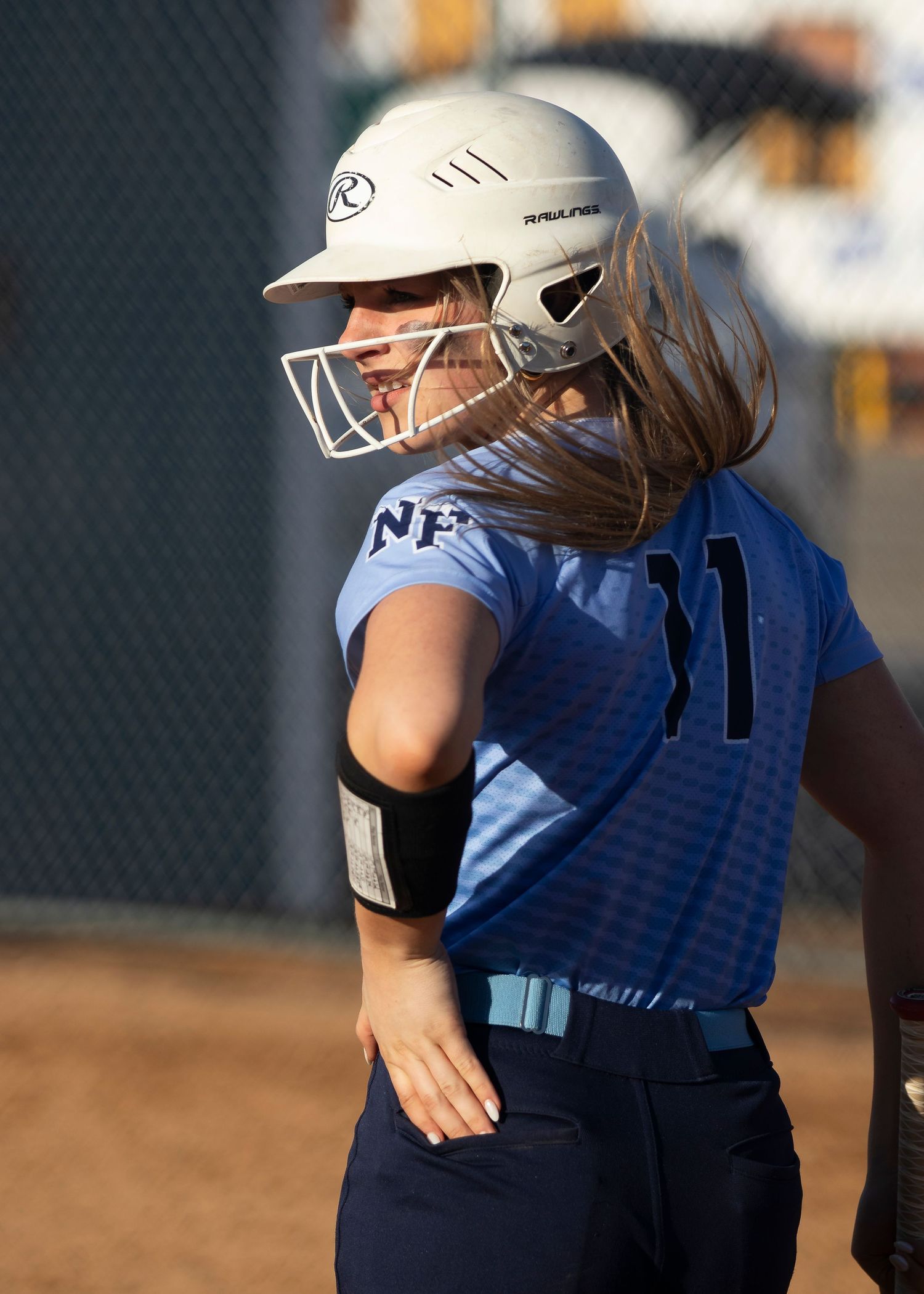 Female softball player in blue NP jersey and white Rawlings batting helmet with face guard.
