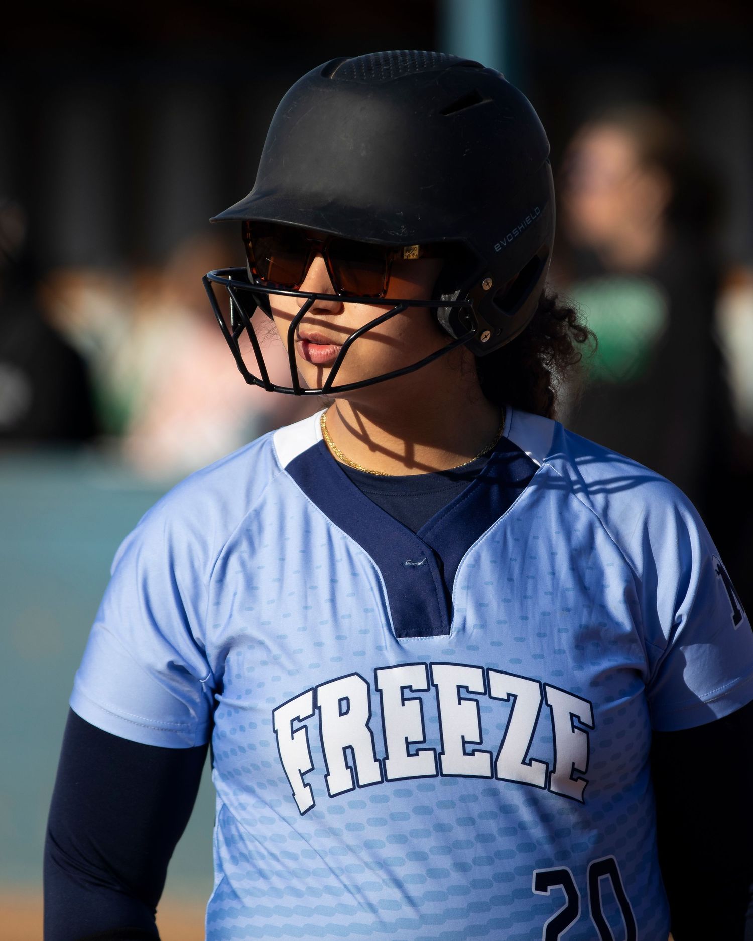 Softball player in blue Freeze jersey and black batting helmet with face guard on the field.