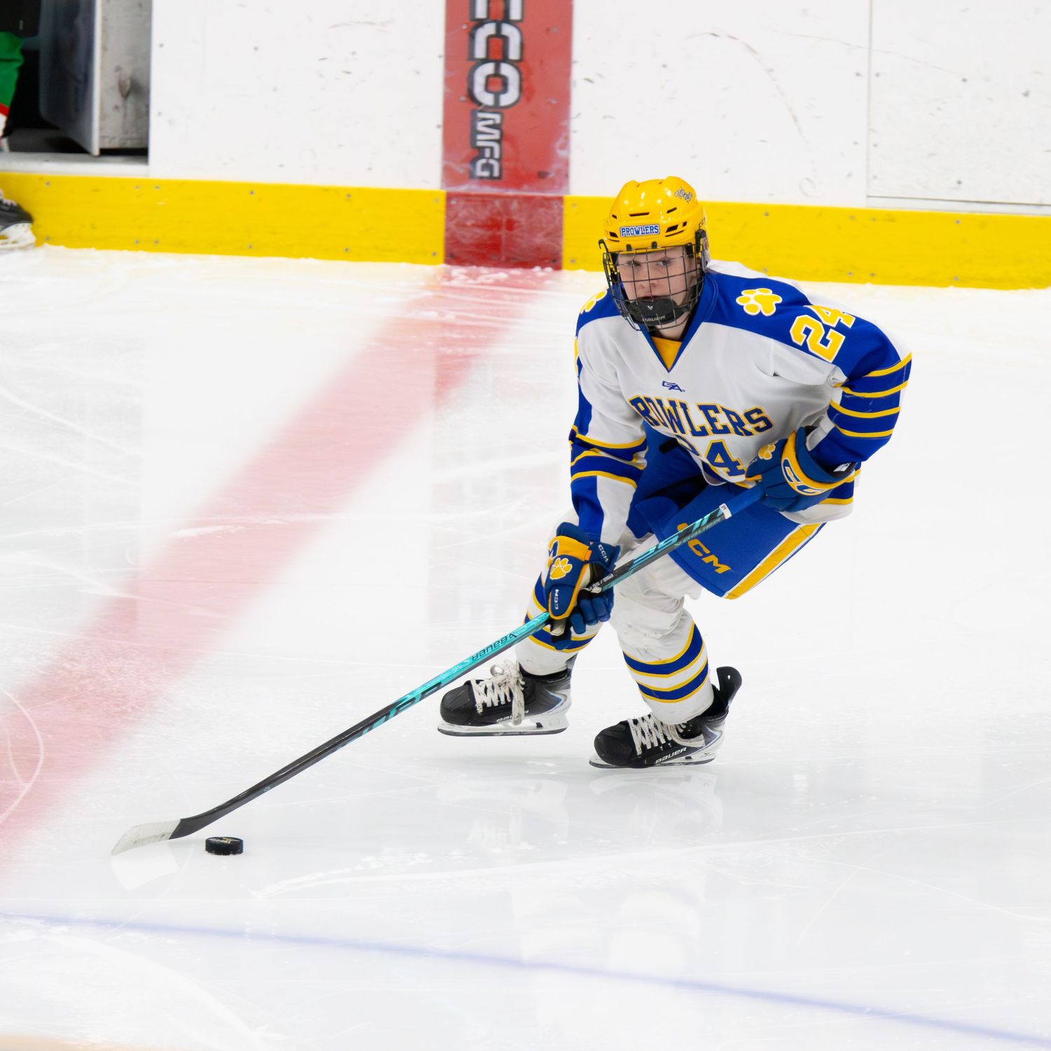 Female hockey player in blue and yellow Boilers jersey skates with puck.