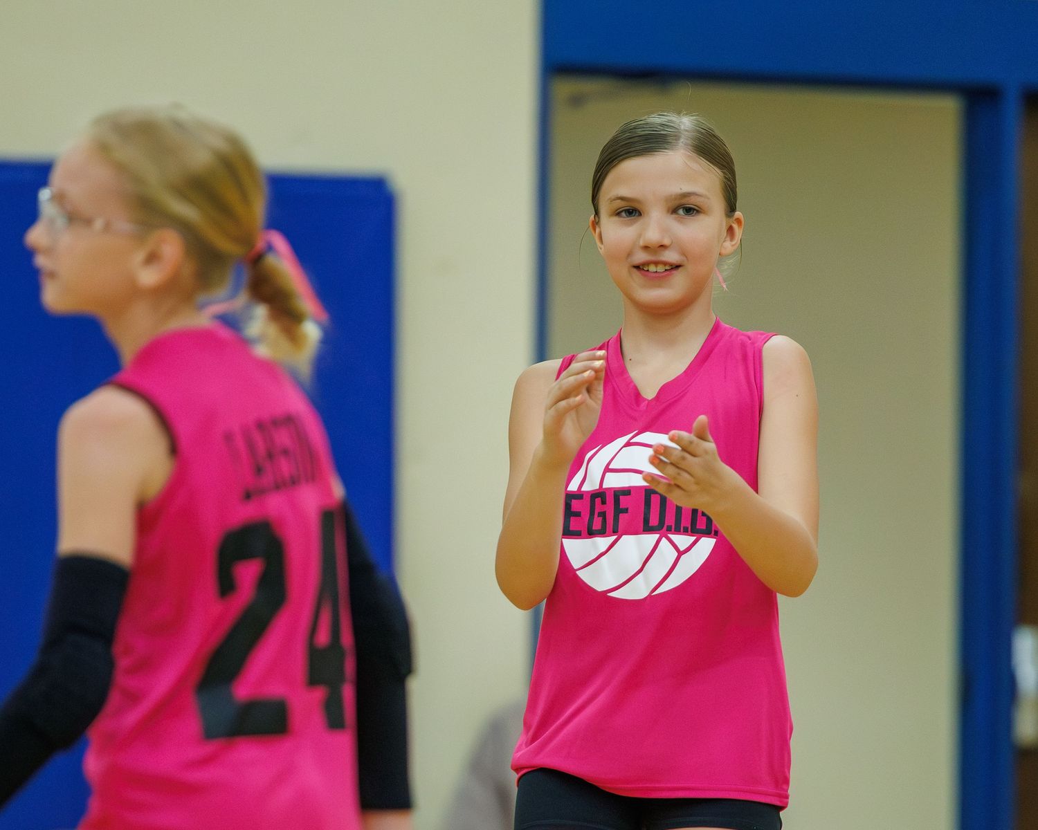 Young girls in pink jerseys playing volleyball at indoor youth sports practice.