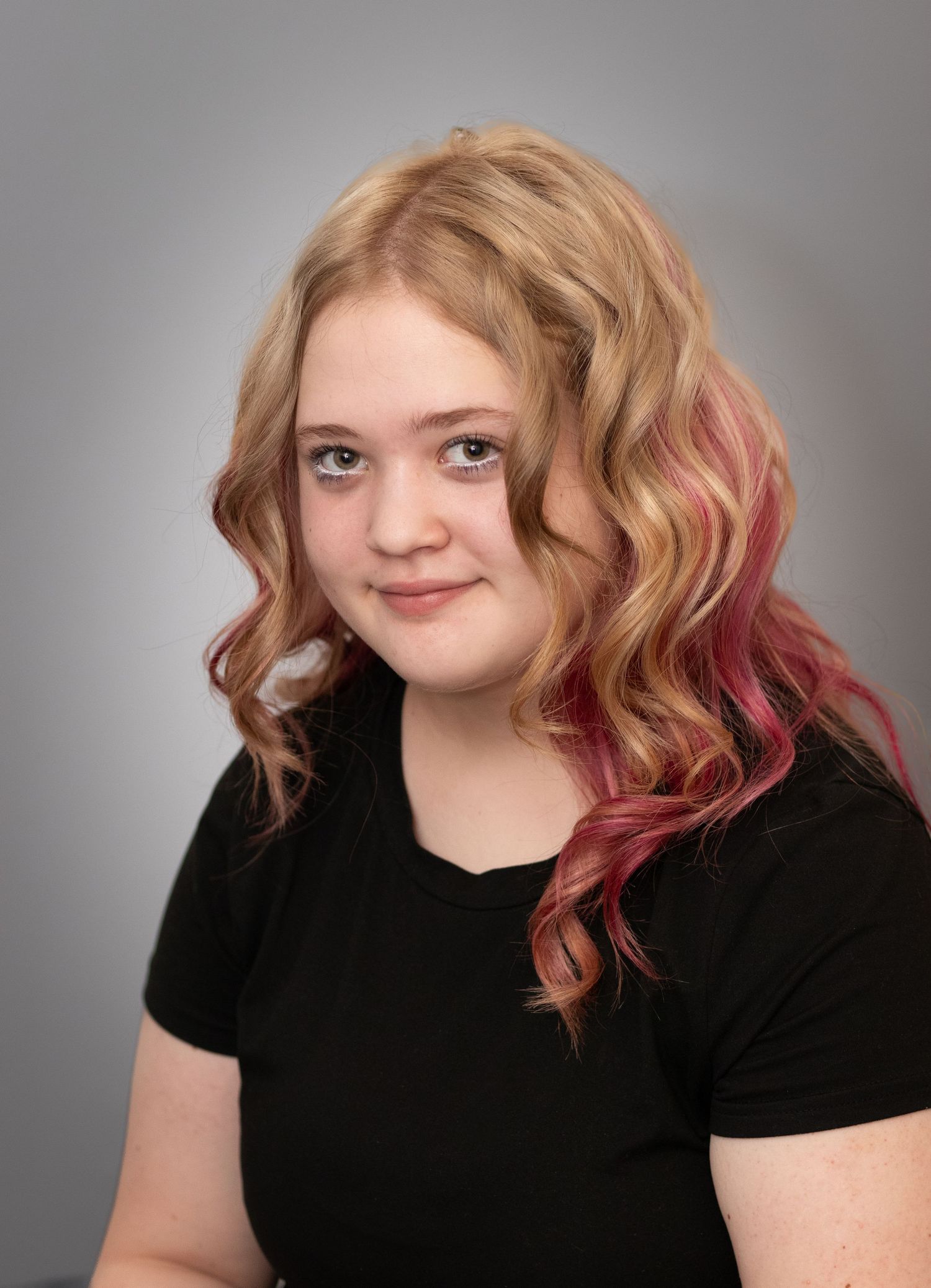 Smiling young woman with long wavy blonde and pink ombre hair wearing a black t-shirt.