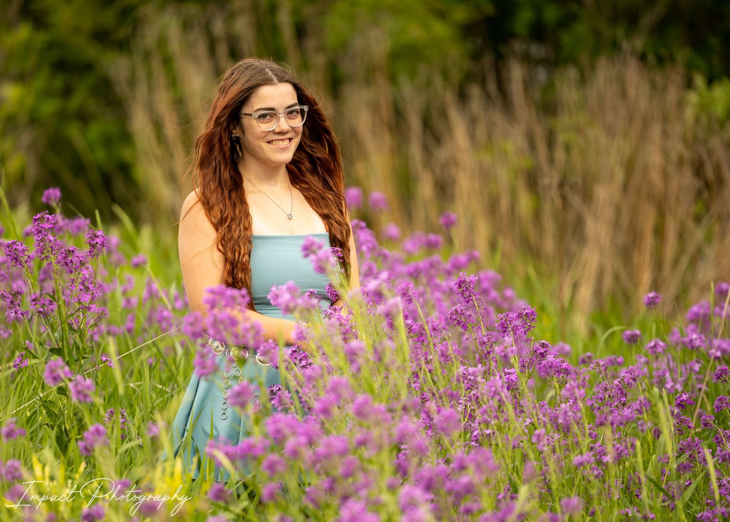 Young woman in blue dress smiling among vibrant purple wildflowers in a lush green field.