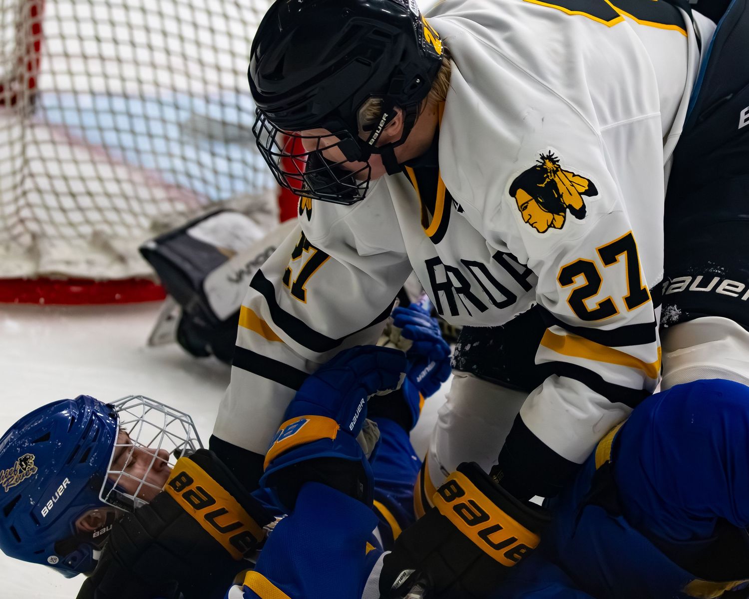 Hockey player number 27 in white jersey pins opponent to ice during intense youth hockey game.