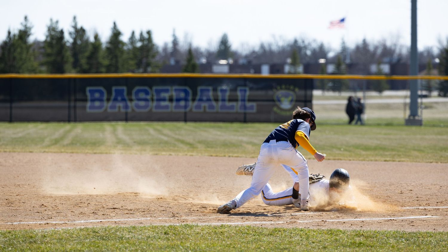 Baseball player sliding into base with dust cloud on dirt infield during outdoor game.