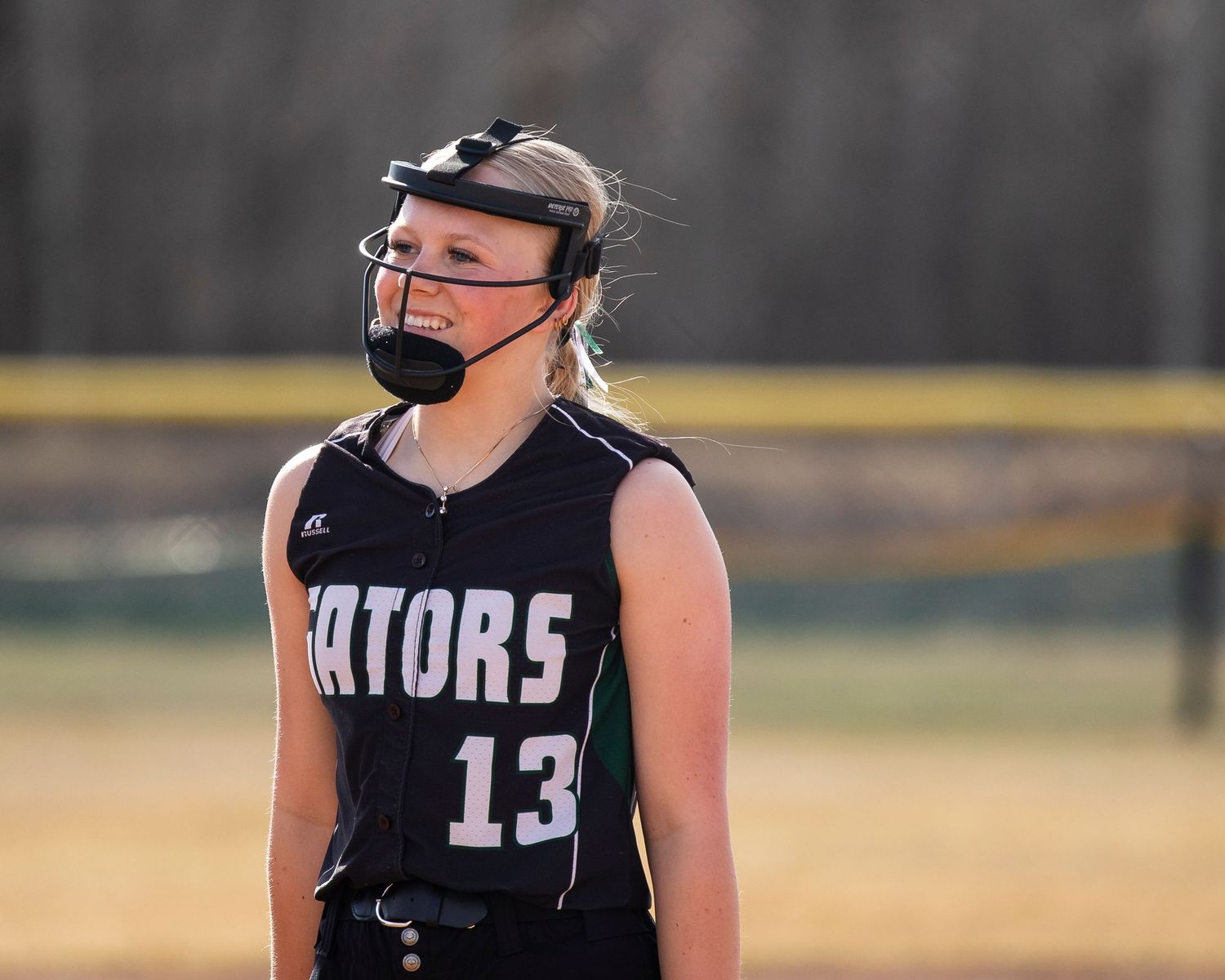 Female softball player #13 in Gators uniform wearing face mask on field during game.