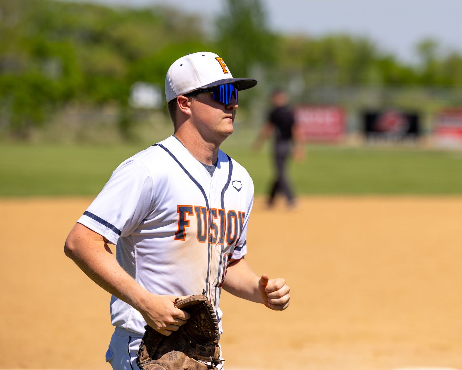 Baseball player in Fusion uniform and sunglasses jogging on field during sunny day game.