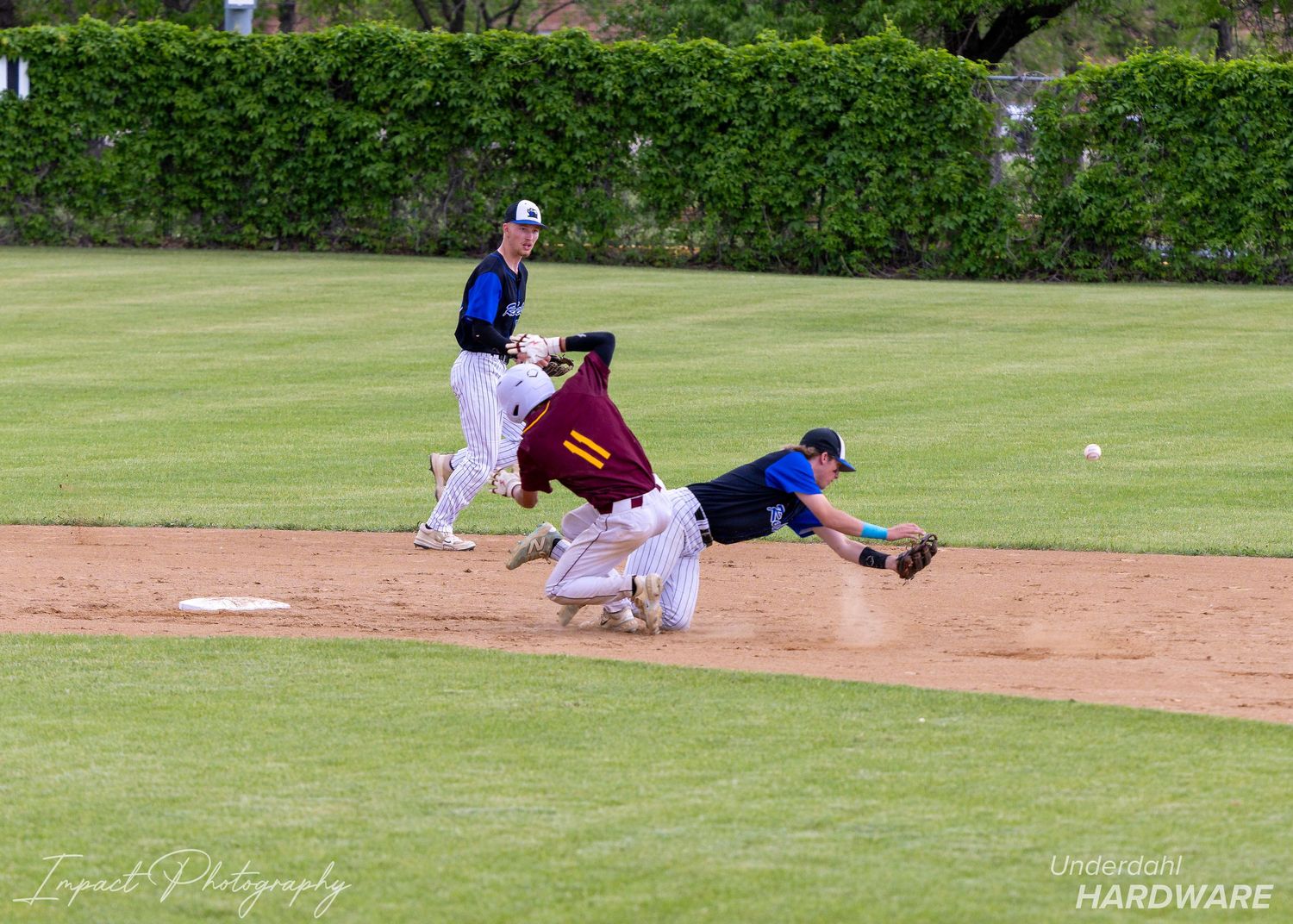 Baseball player diving to second base during a game while infielder attempts to make the tag on a sunny day.