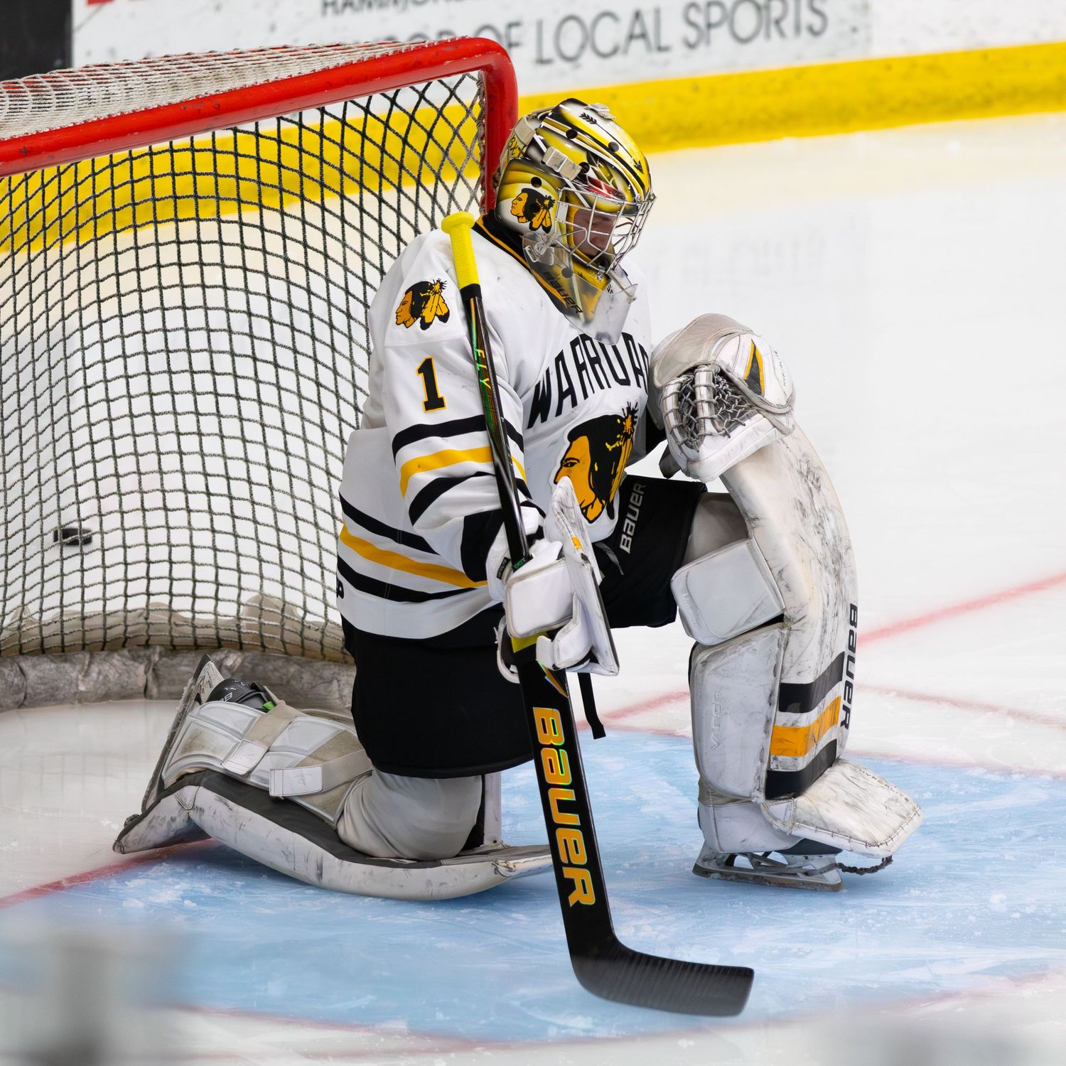 Ice hockey goalie in yellow and black Warriors uniform kneeling in front of the net.
