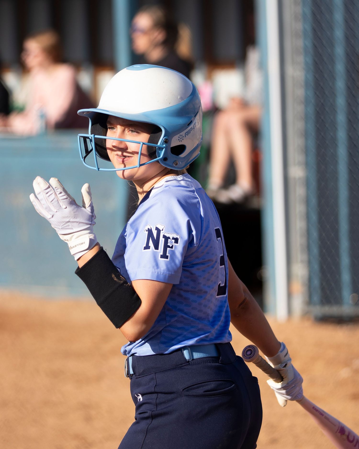 Female softball player in NF blue uniform and helmet holds bat ready at plate during sunny game.