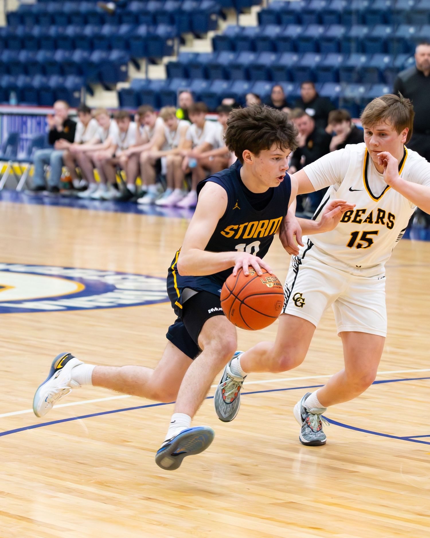 Storm basketball player number 10 drives past Bears defender number 15 during indoor basketball game.
