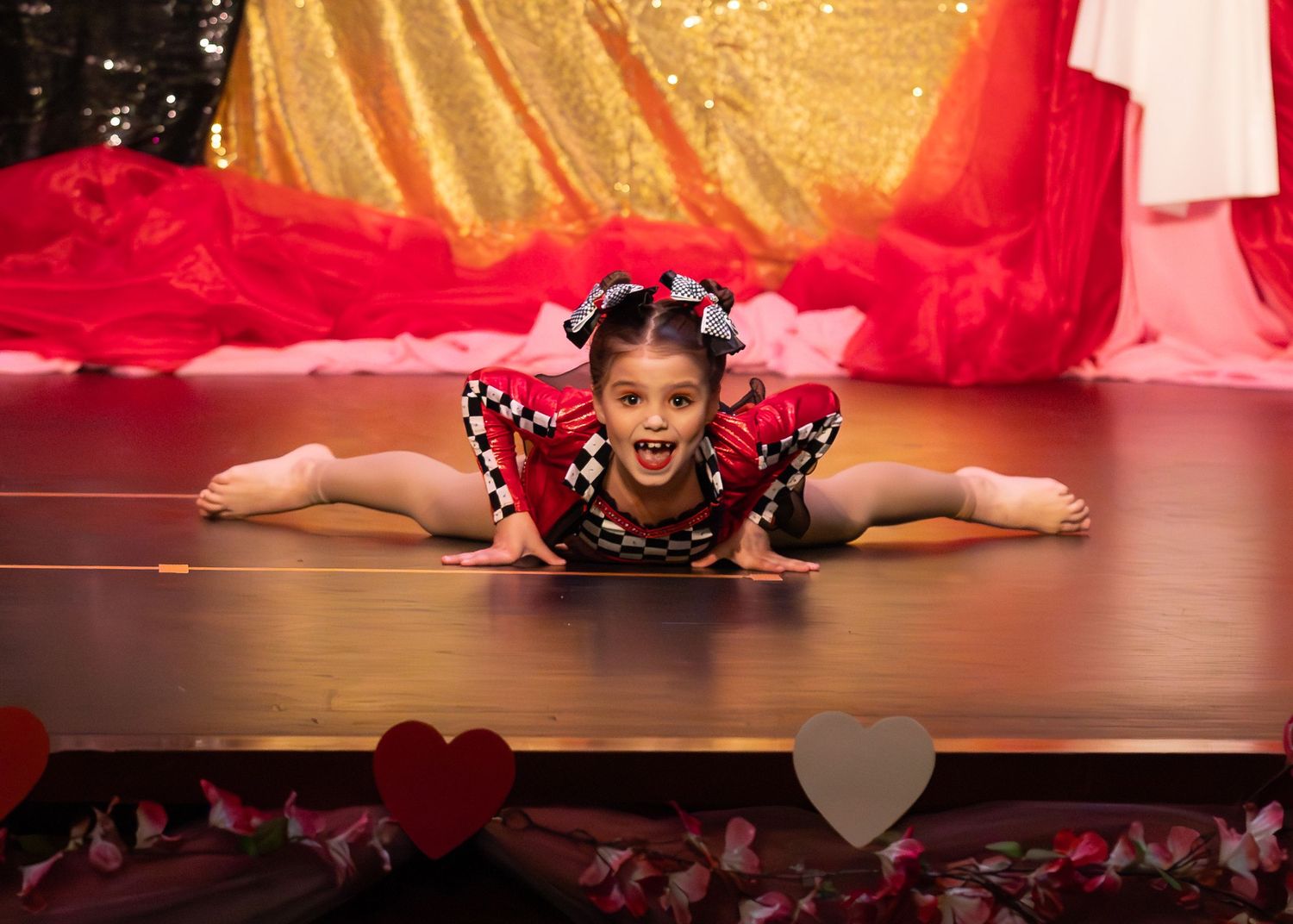 Young girl in checkered costume doing a split on stage during a dance recital performance.