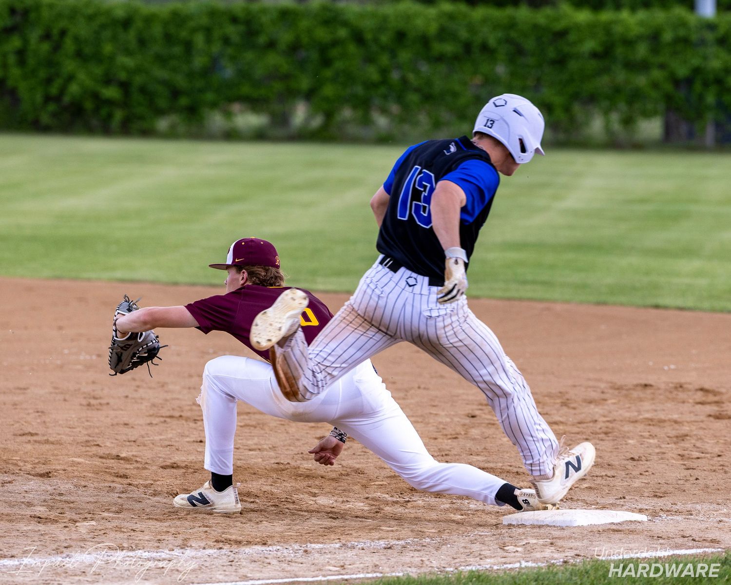 Baseball player in white uniform #13 rounds base as maroon-clad fielder reaches to make the tag during a game.