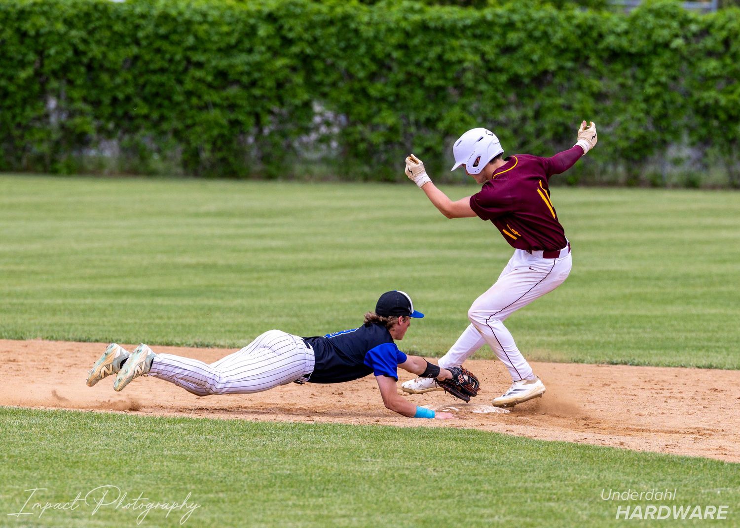 Baseball player dives back to base as infielder leaps to catch the ball during a youth baseball game.