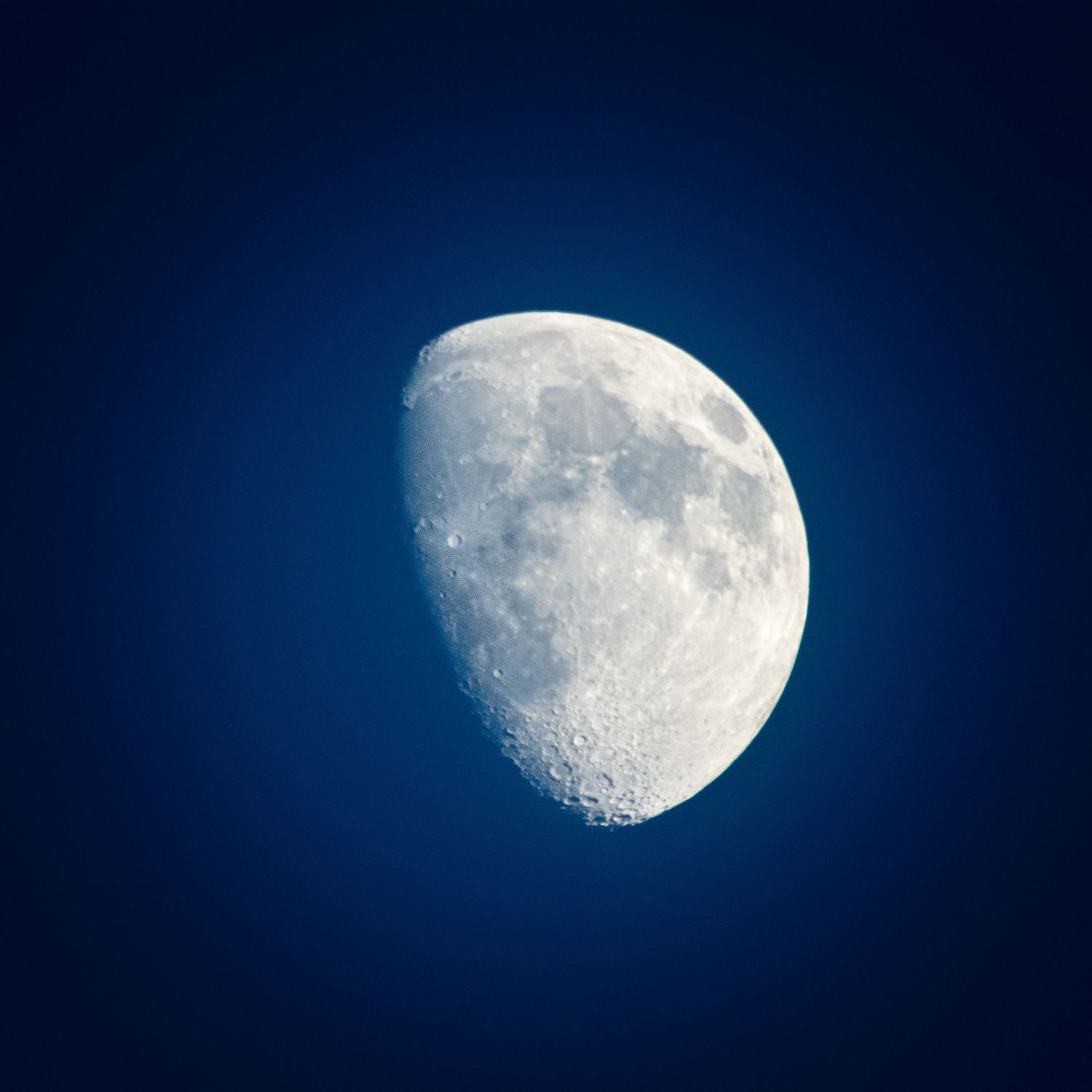 Close-up photo of a waxing gibbous moon against a deep blue sky.