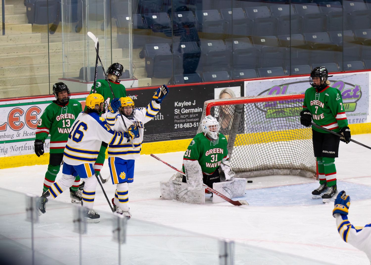 Girls hockey players celebrate goal against Green team goalie on ice.