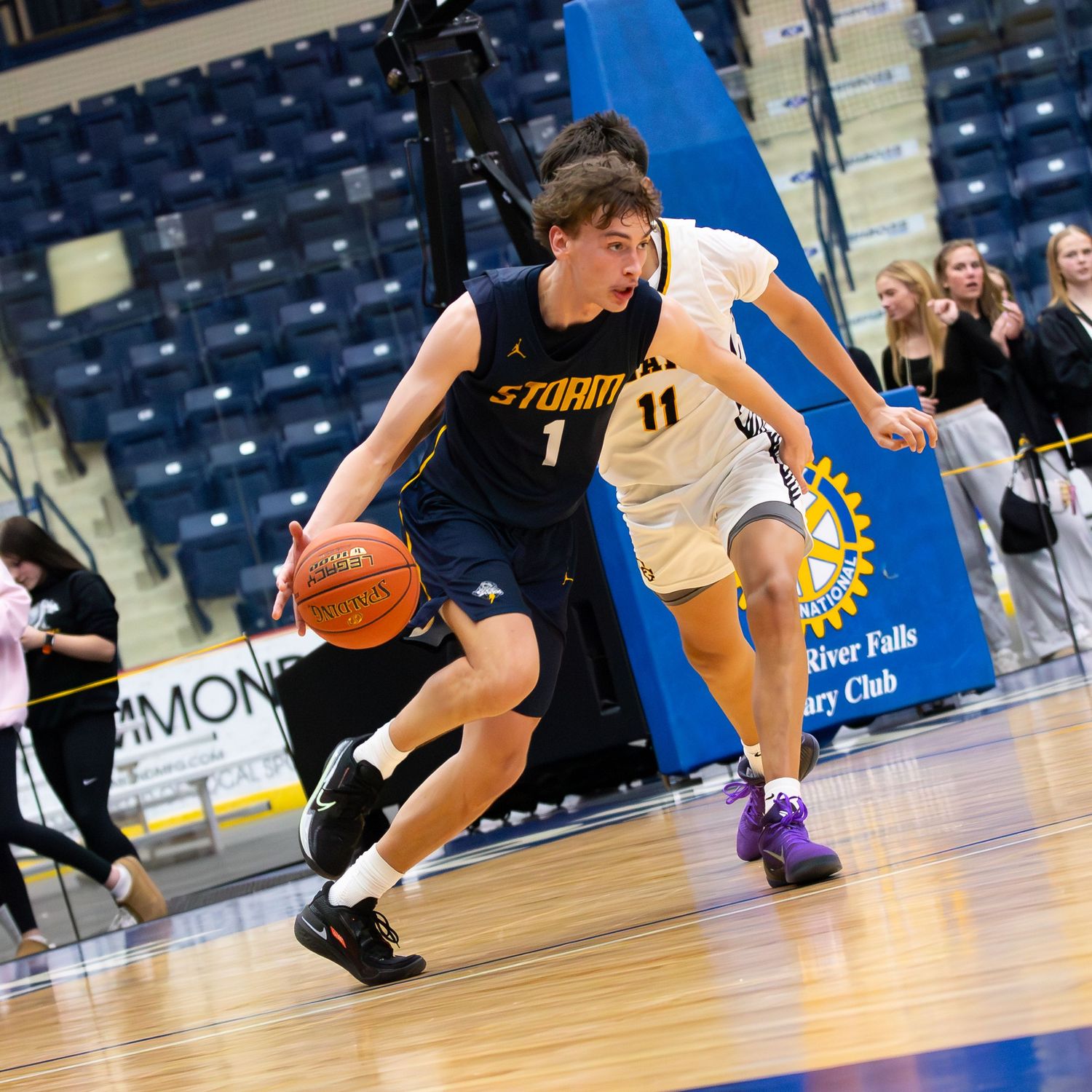 Player #1 in navy Storm jersey dribbles past defender #11 during high school basketball game.