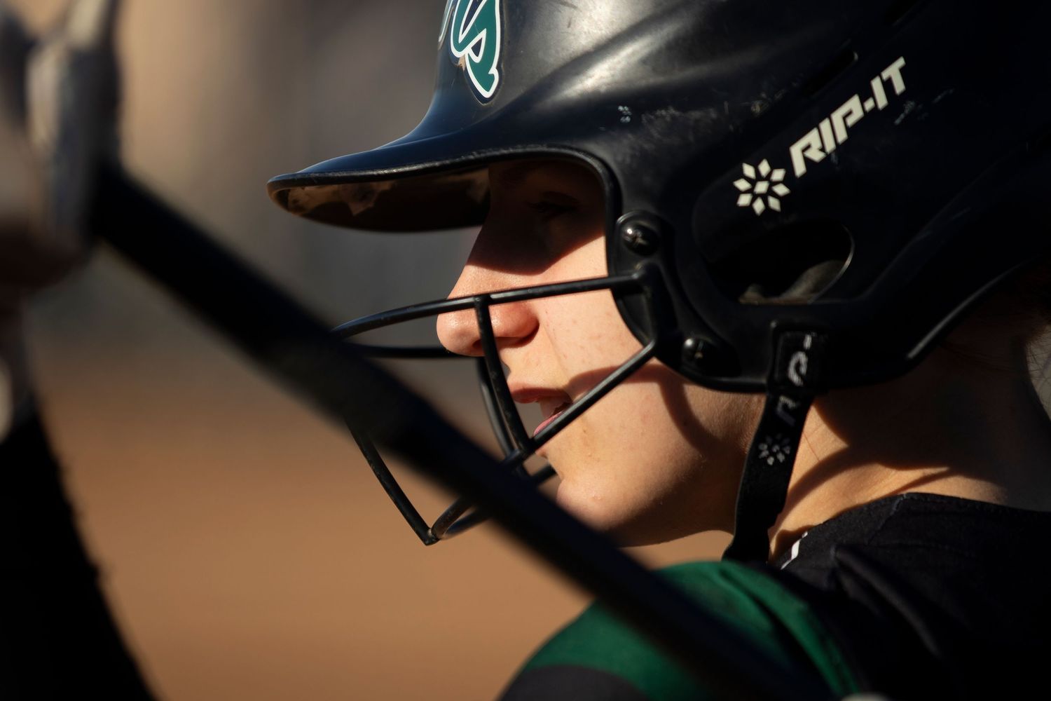 Close-up of a softball player wearing a black RIP-IT batting helmet with face guard during a game.