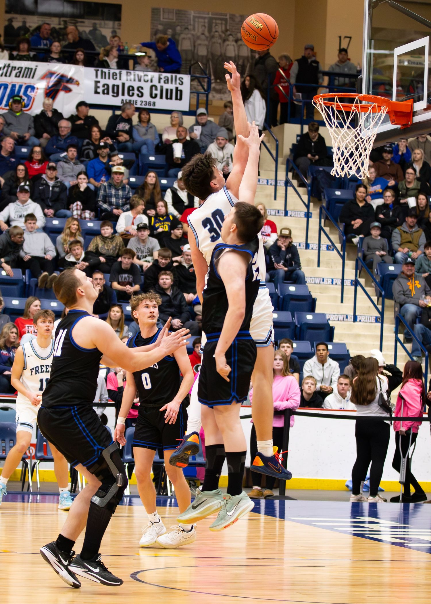 High school basketball player #30 attempts a layup over defenders in a packed gym at Thief River Falls Eagles Club.