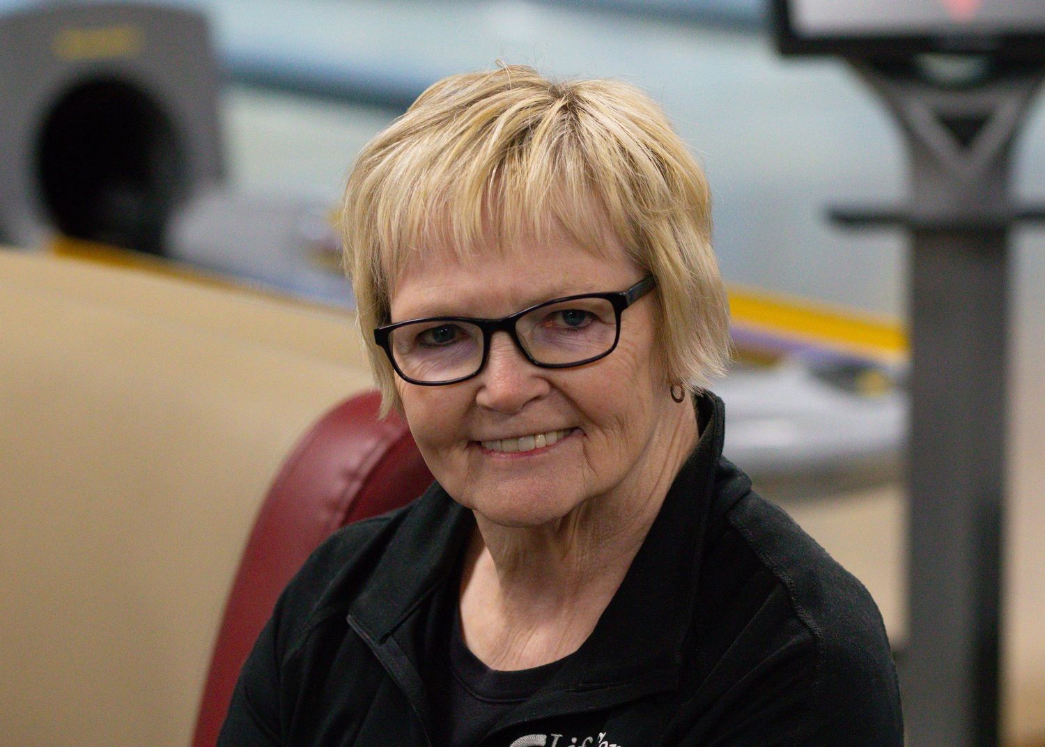 Smiling older woman with short blonde hair and glasses wearing a black top.
