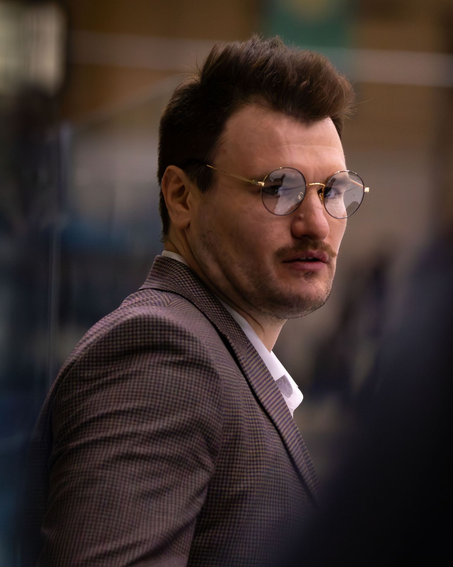 Coach with mustache wearing round glasses and checkered blazer.