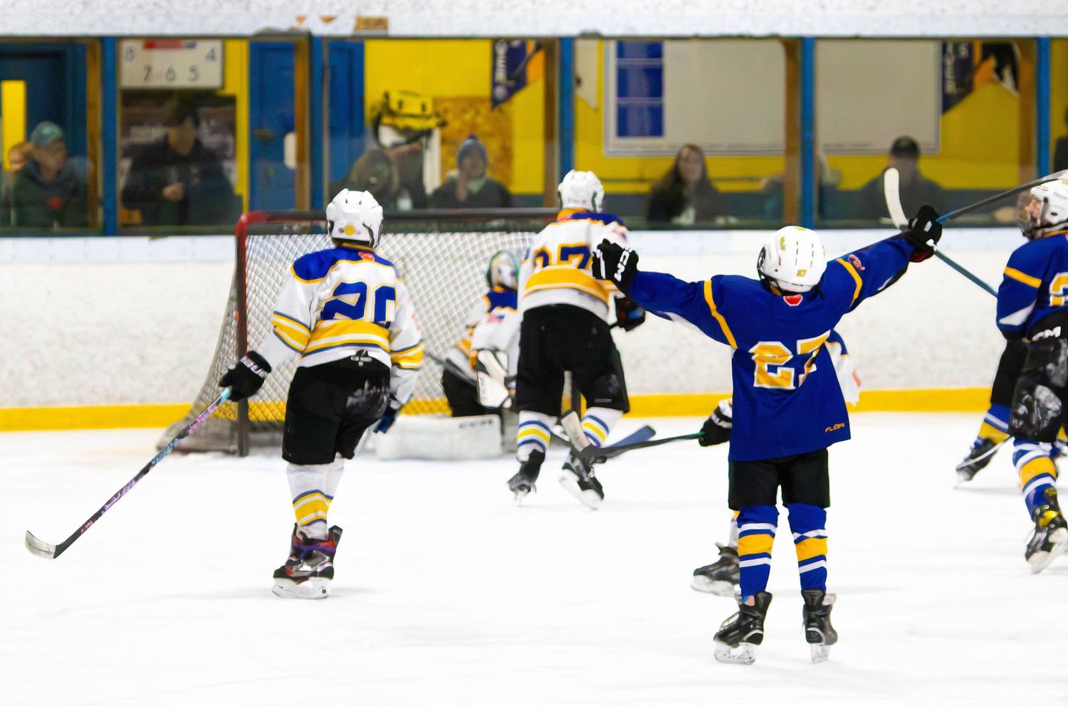 Youth hockey players in blue and yellow celebrate a goal scored against opposing team in white and blue jerseys. Prowlers.