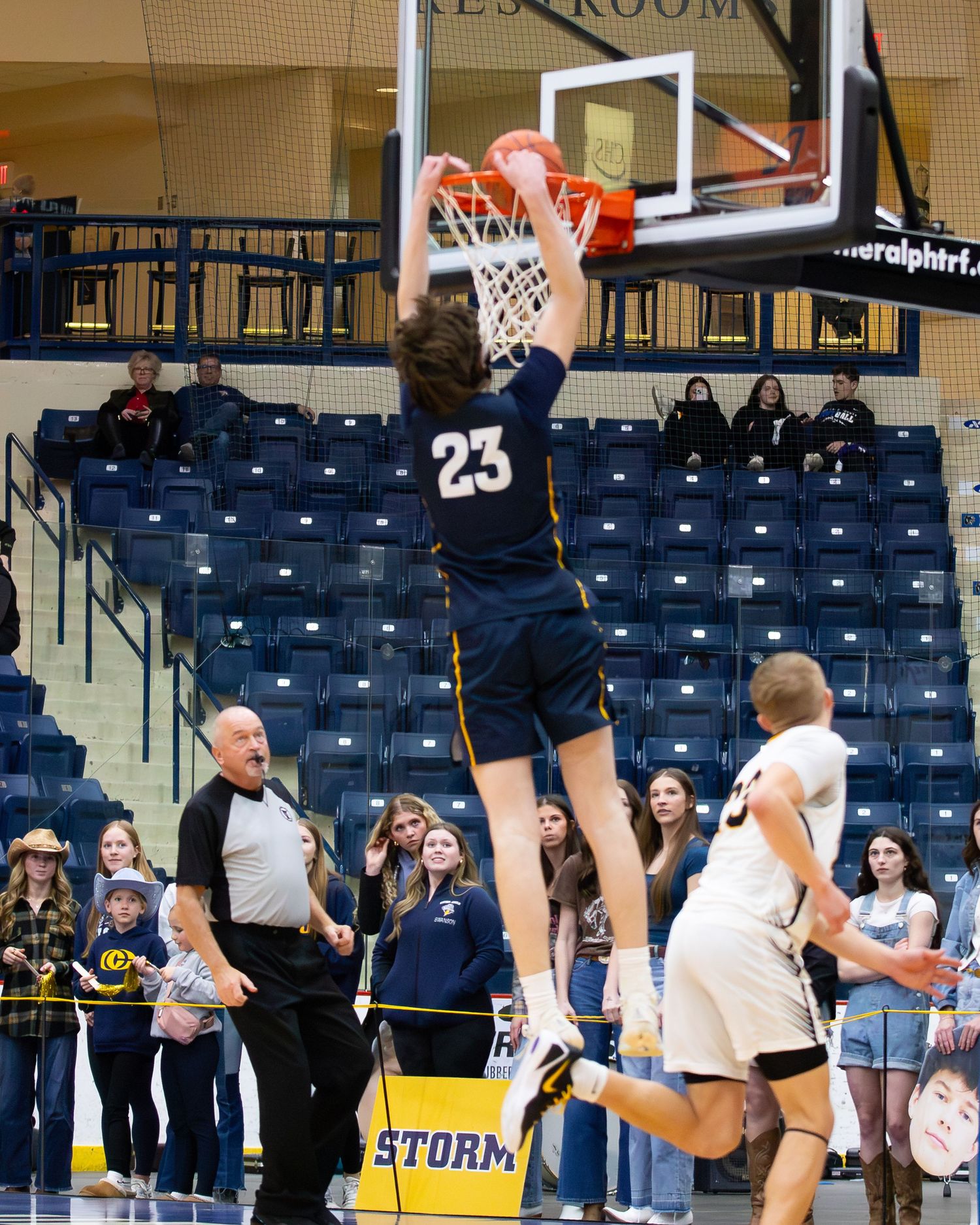 Storm basketball player number 23 dunks ball during exciting high school basketball game.