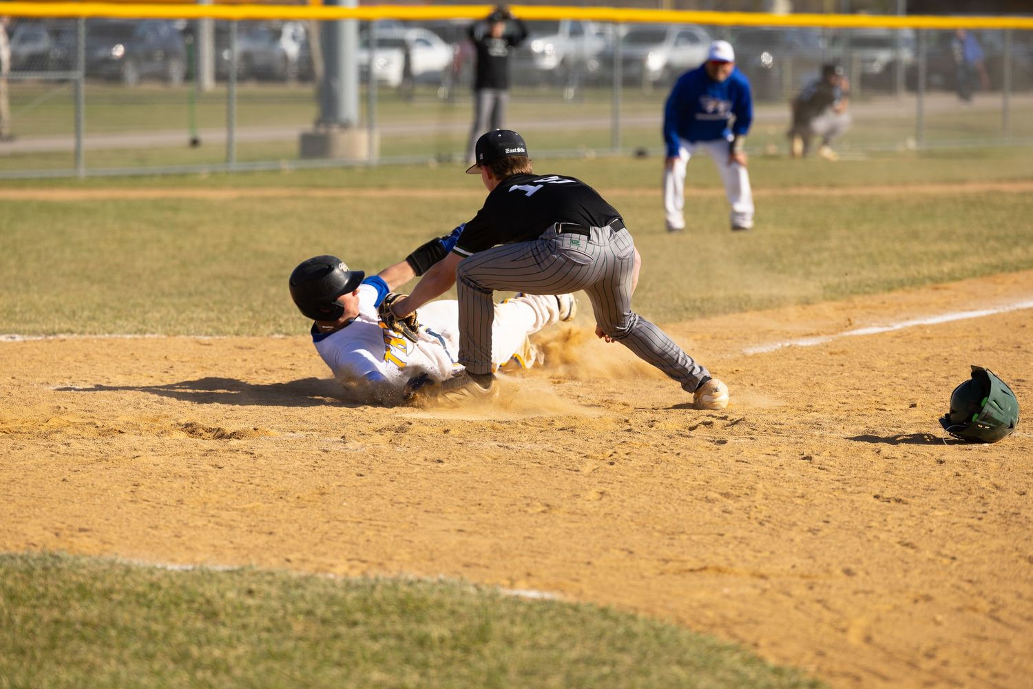 Baseball player sliding into base as fielder applies tag in dusty infield during youth league game.