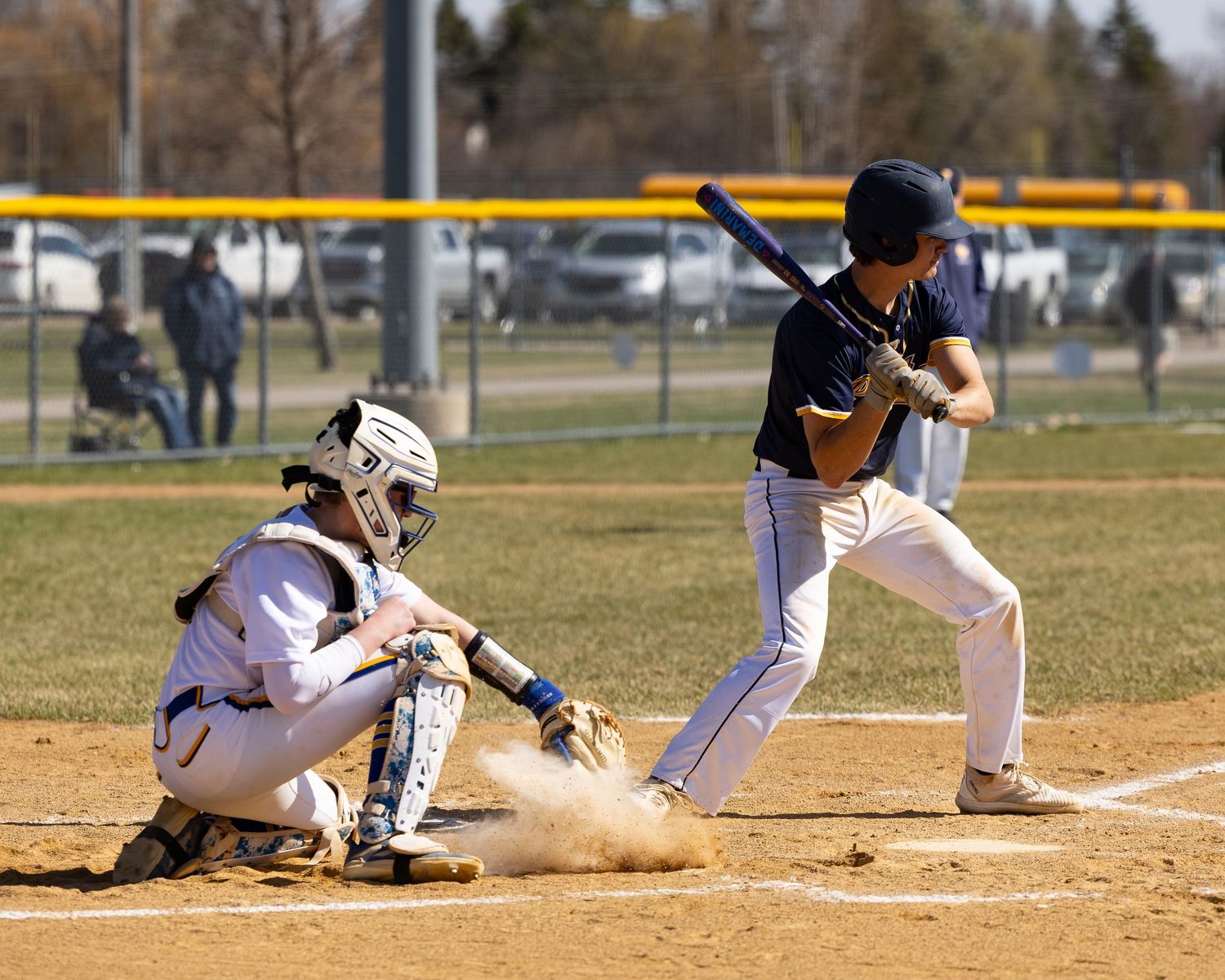Baseball batter prepares to swing at home plate as catcher crouches in position during a sunny outdoor game.