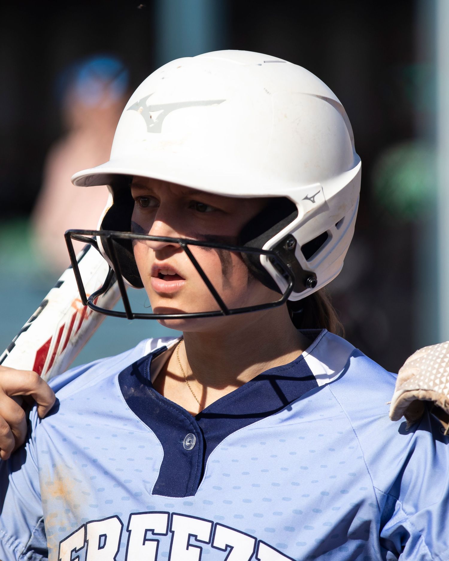 Young softball player wearing a white Mizuno batting helmet with face guard in a light blue jersey.