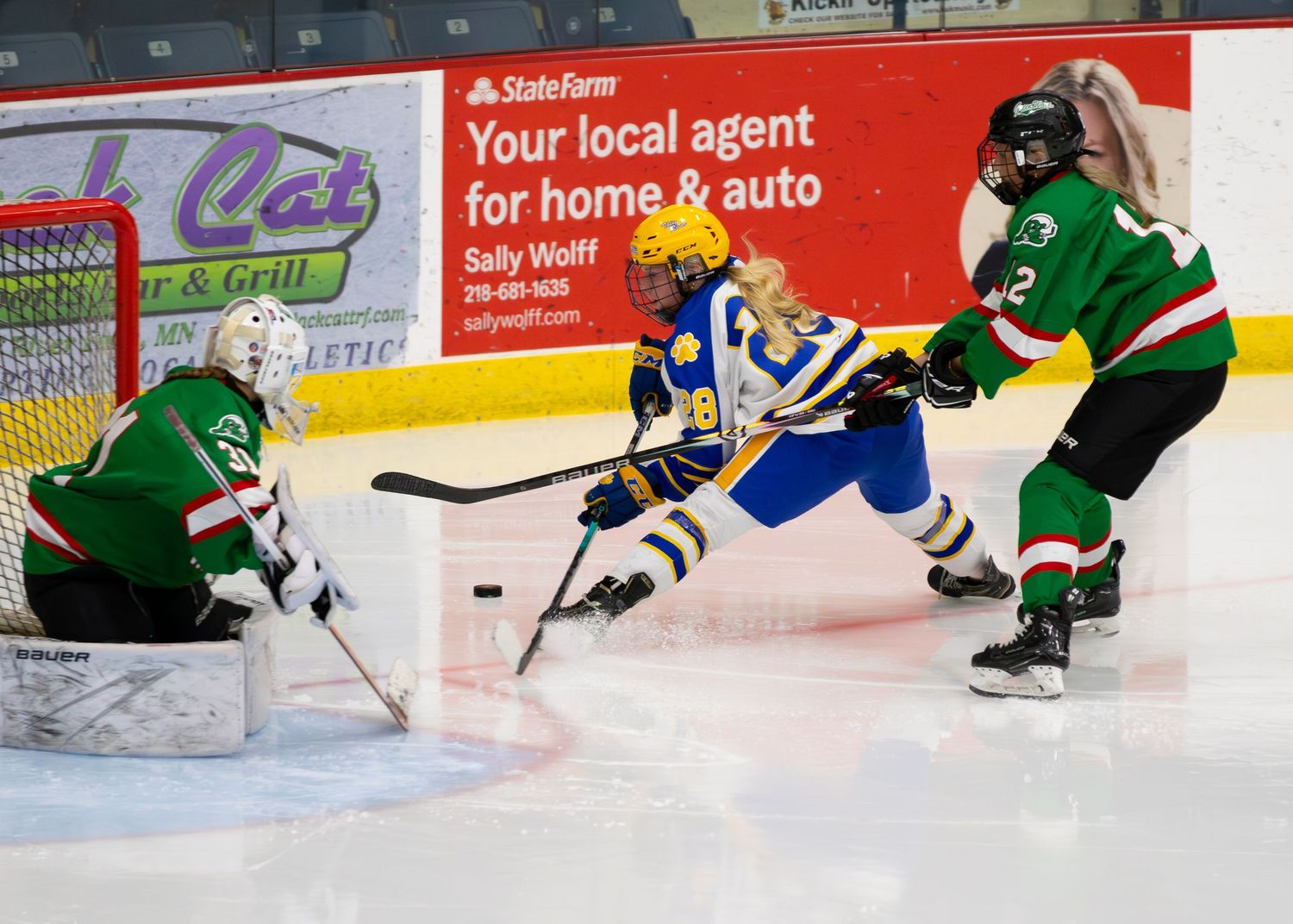 Girls hockey player in blue drives toward goal past Green team goalie.