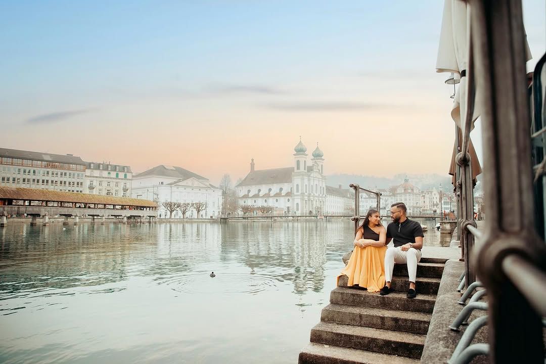 Couple sitting on waterfront steps at sunset in Lucerne, Switzerland, with historic buildings reflecting on the calm lake.