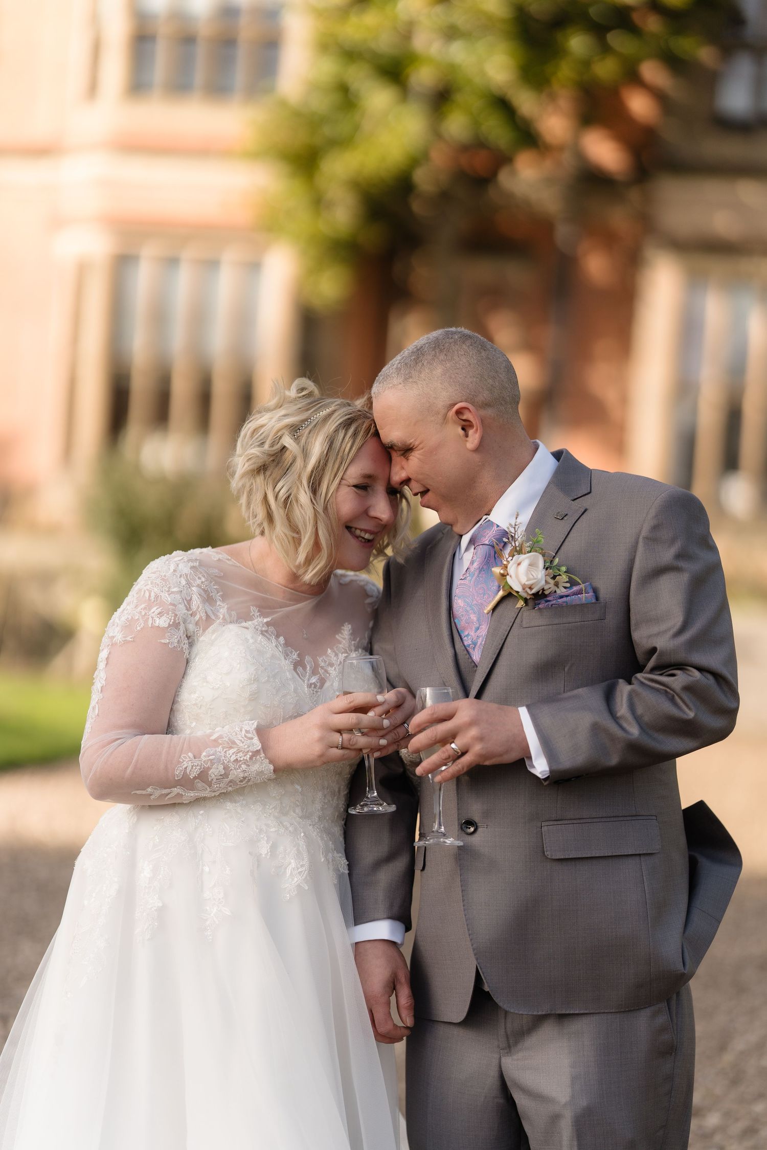 Bride and groom share a tender moment holding champagne glasses outside a grand venue on their wedding day.