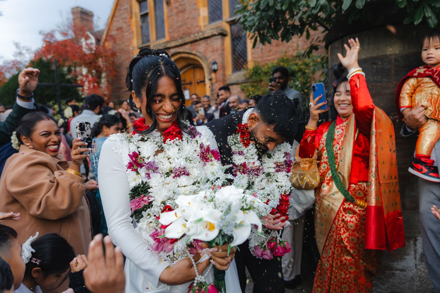 Bride in white dress wearing floral garland celebrating outside historic church.