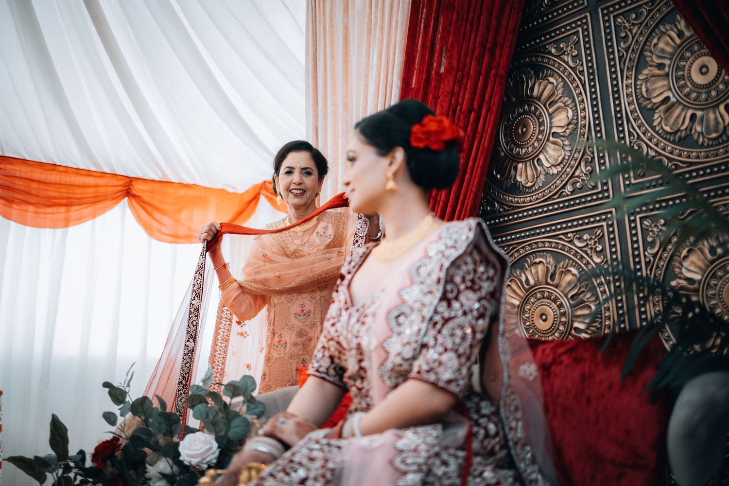 Two women in traditional Indian attire at a wedding celebration with decorative backdrop.