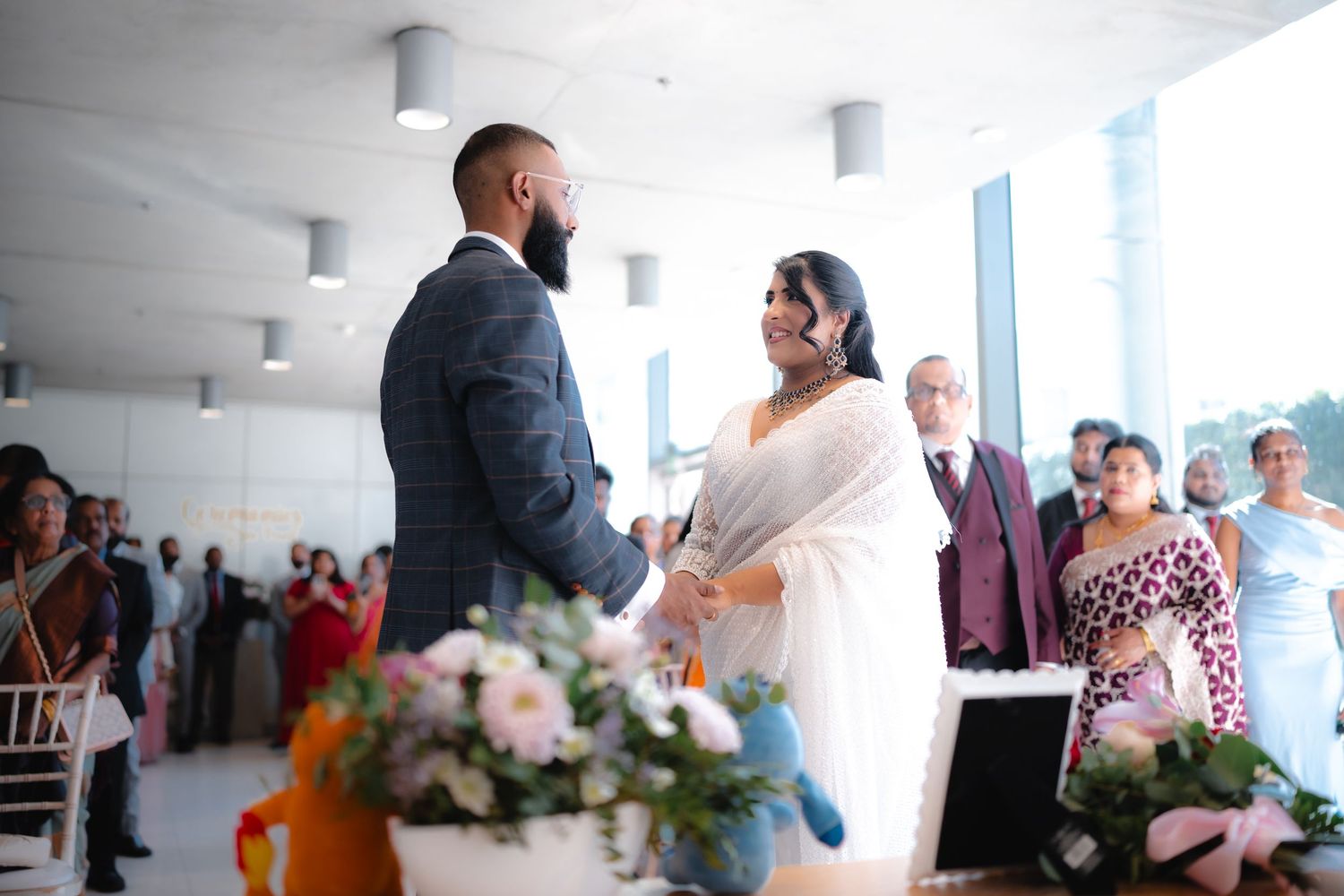 Bride and groom exchange vows at modern wedding ceremony venue with guests seated in background.