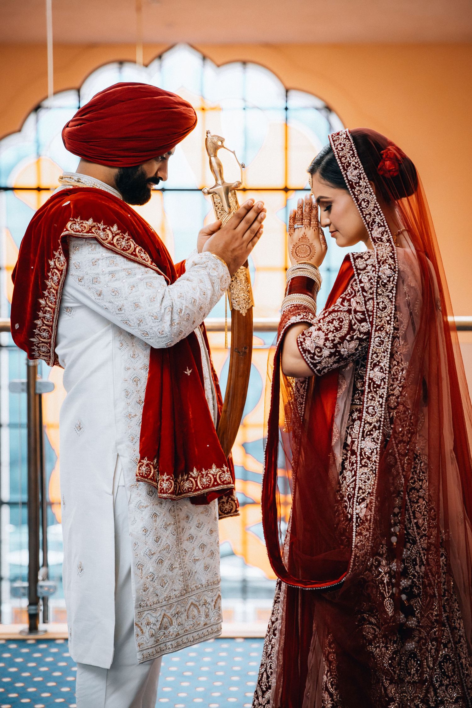 Sikh bride and groom in traditional red and white wedding attire praying together at ceremony.