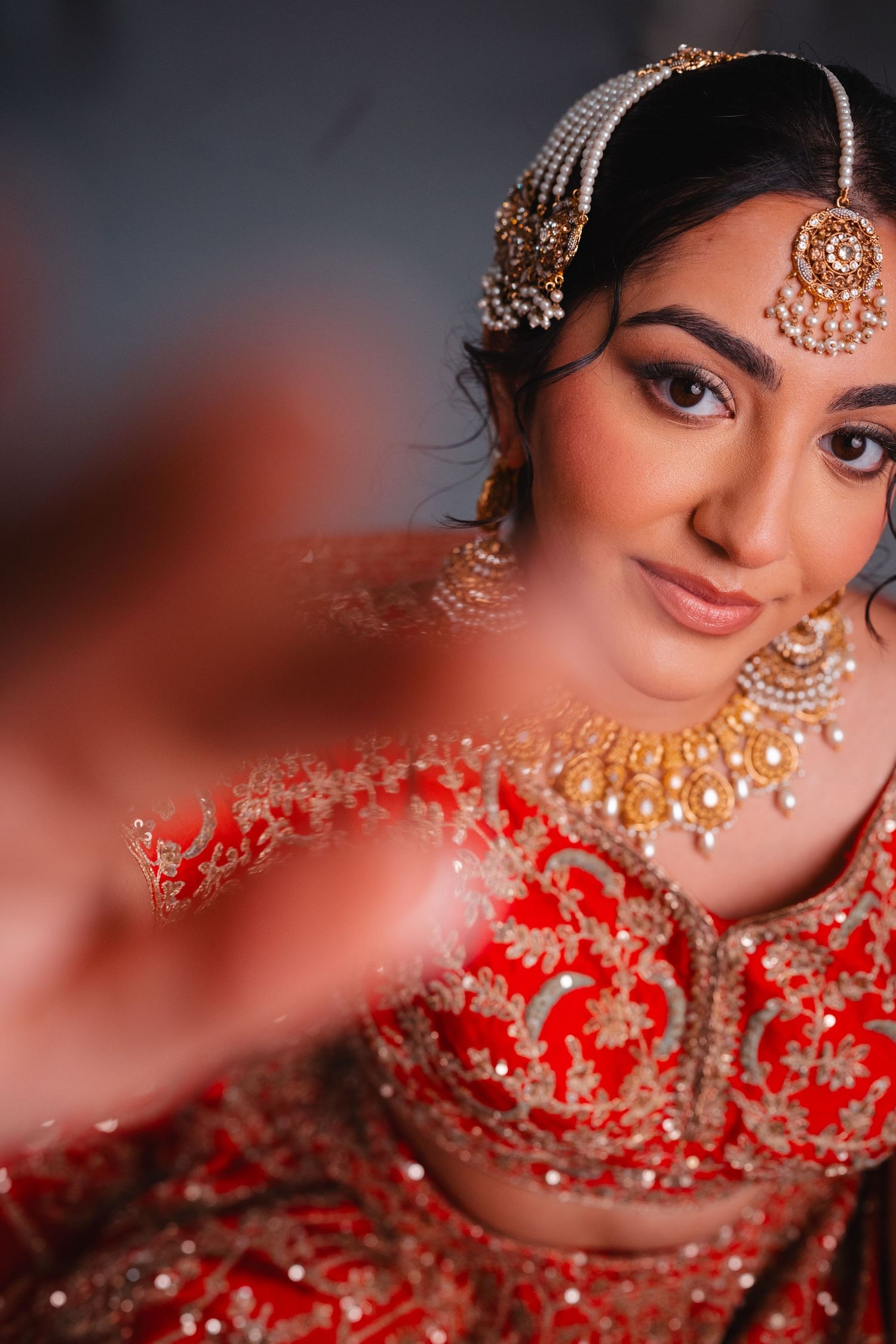 Indian bride in red lehenga with gold jewelry and maang tikka smiling gracefully during bridal portrait session.