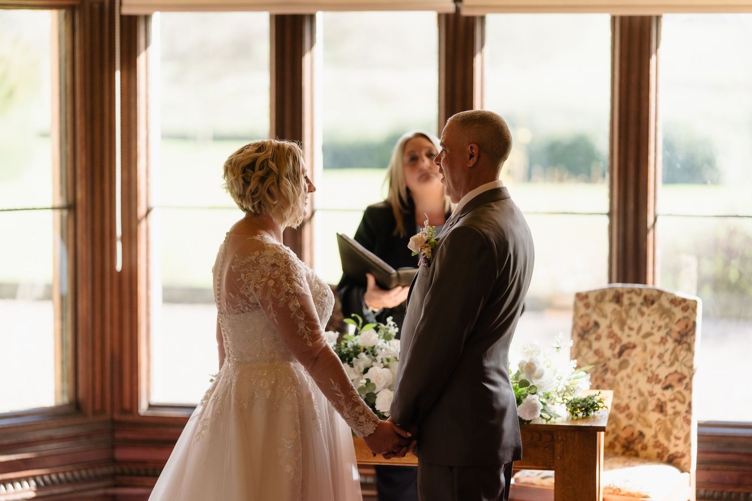 Bride and groom holding hands during intimate wedding ceremony with officiant in elegant venue.