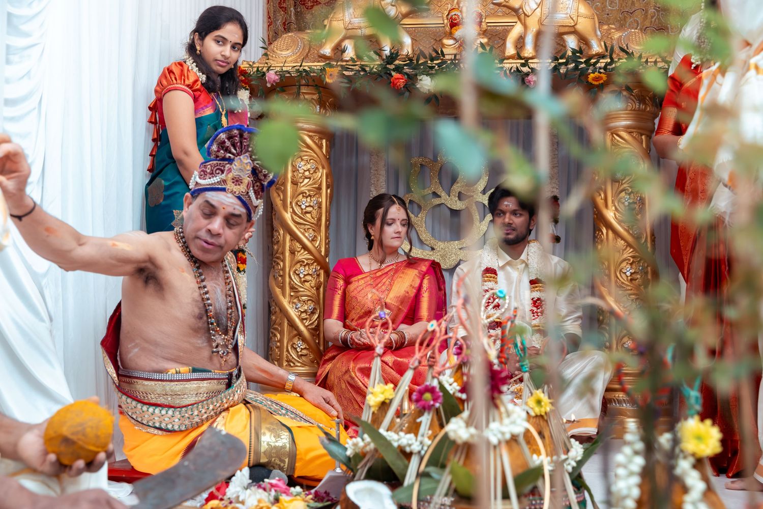 Traditional Hindu wedding ceremony with priest performing rituals as bride and groom sit at decorated altar.