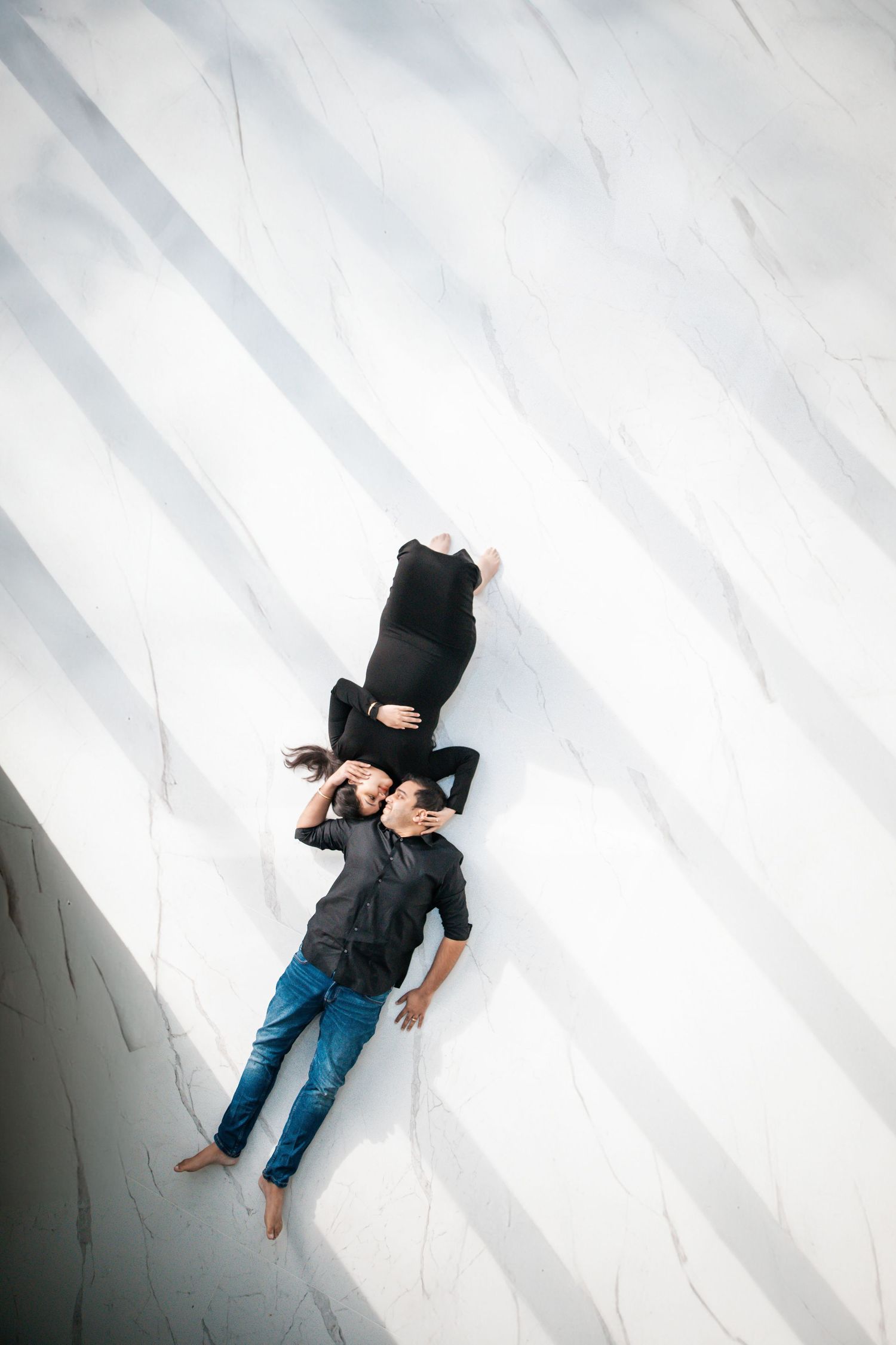 Aerial view of couple lying on white marble surface in matching black outfits.