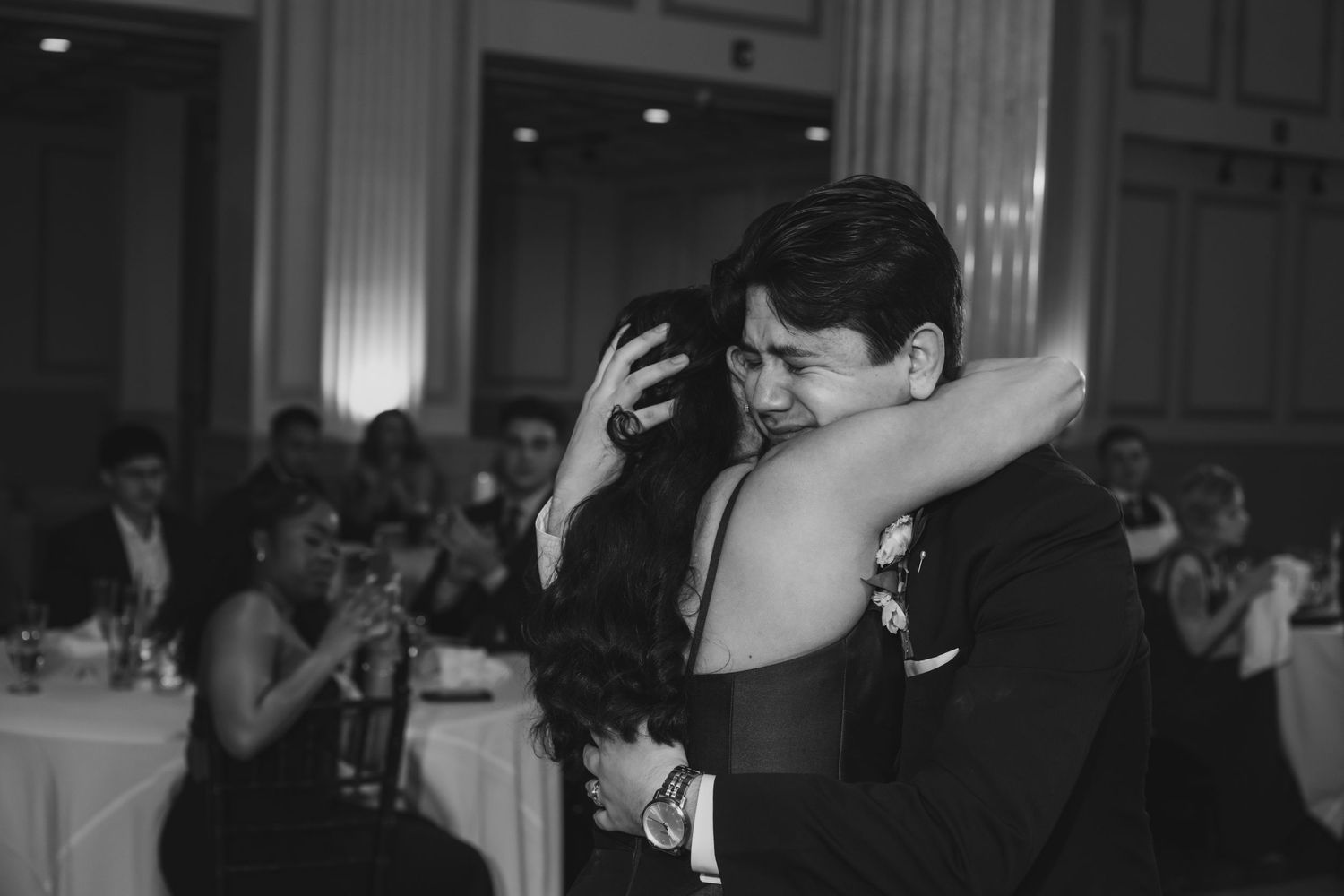 Couple sharing emotional hug on dance floor at elegant wedding reception in black and white photo.