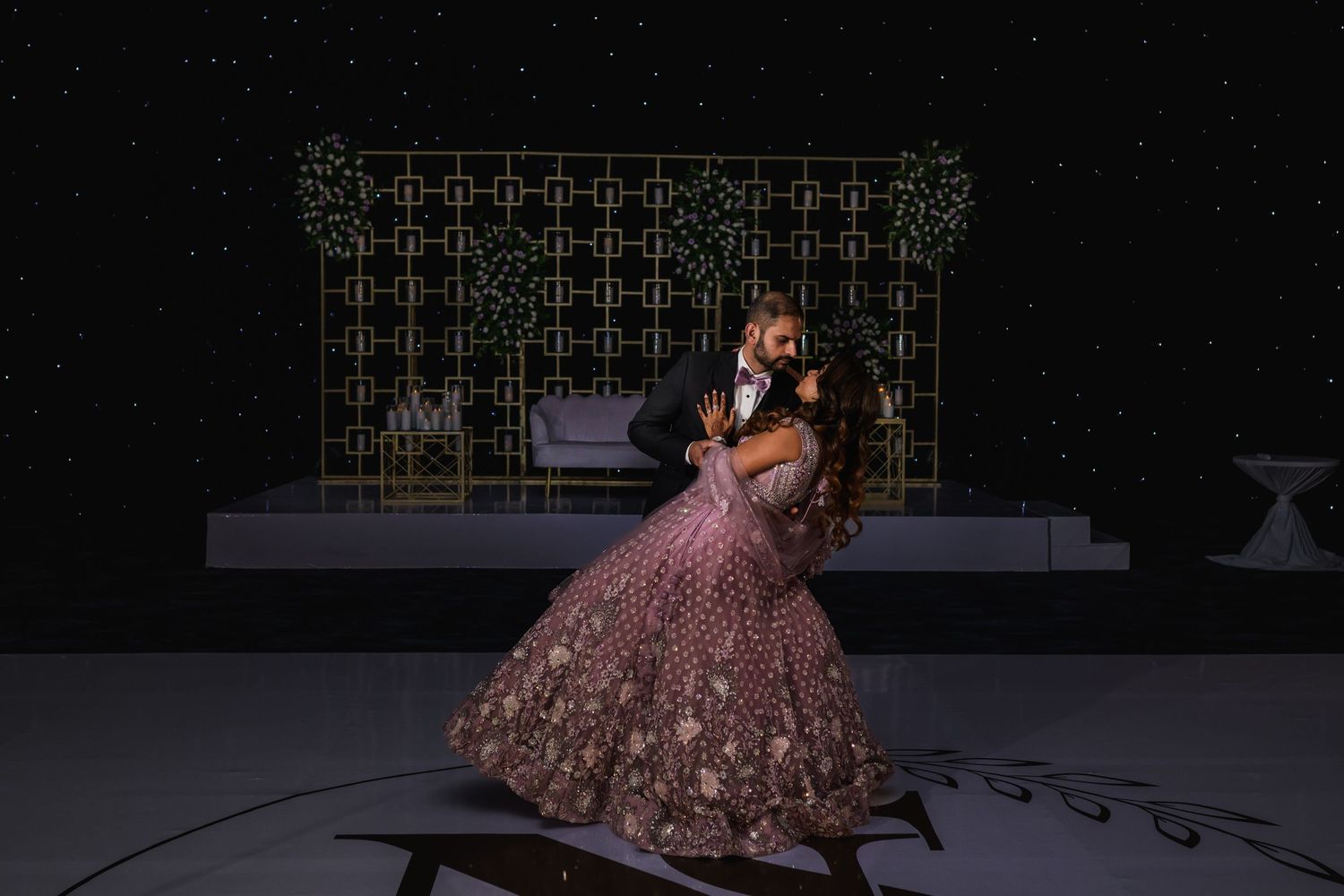 Wedding couple share romantic dance in front of illuminated geometric backdrop at evening reception.