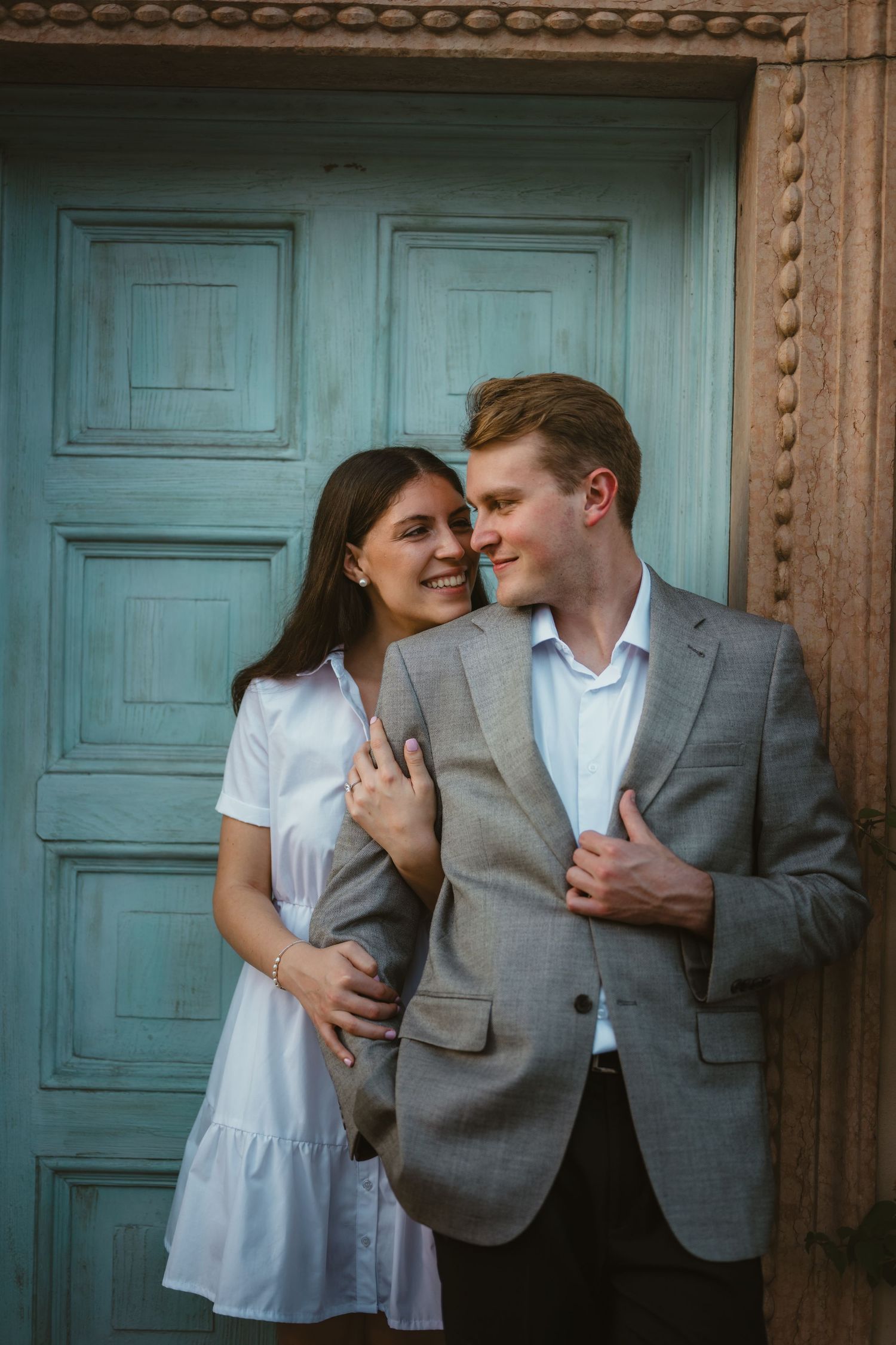 Happy couple posing closely together in front of a rustic turquoise wooden door outdoors.