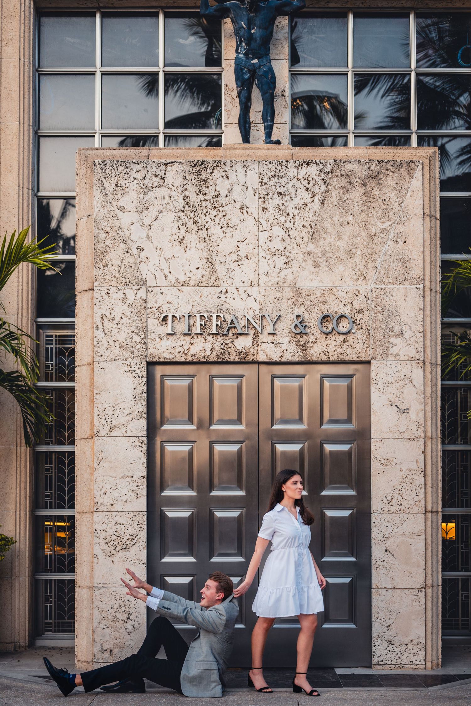 Couple posing playfully in front of Tiffany and Co store entrance with sculptures above.