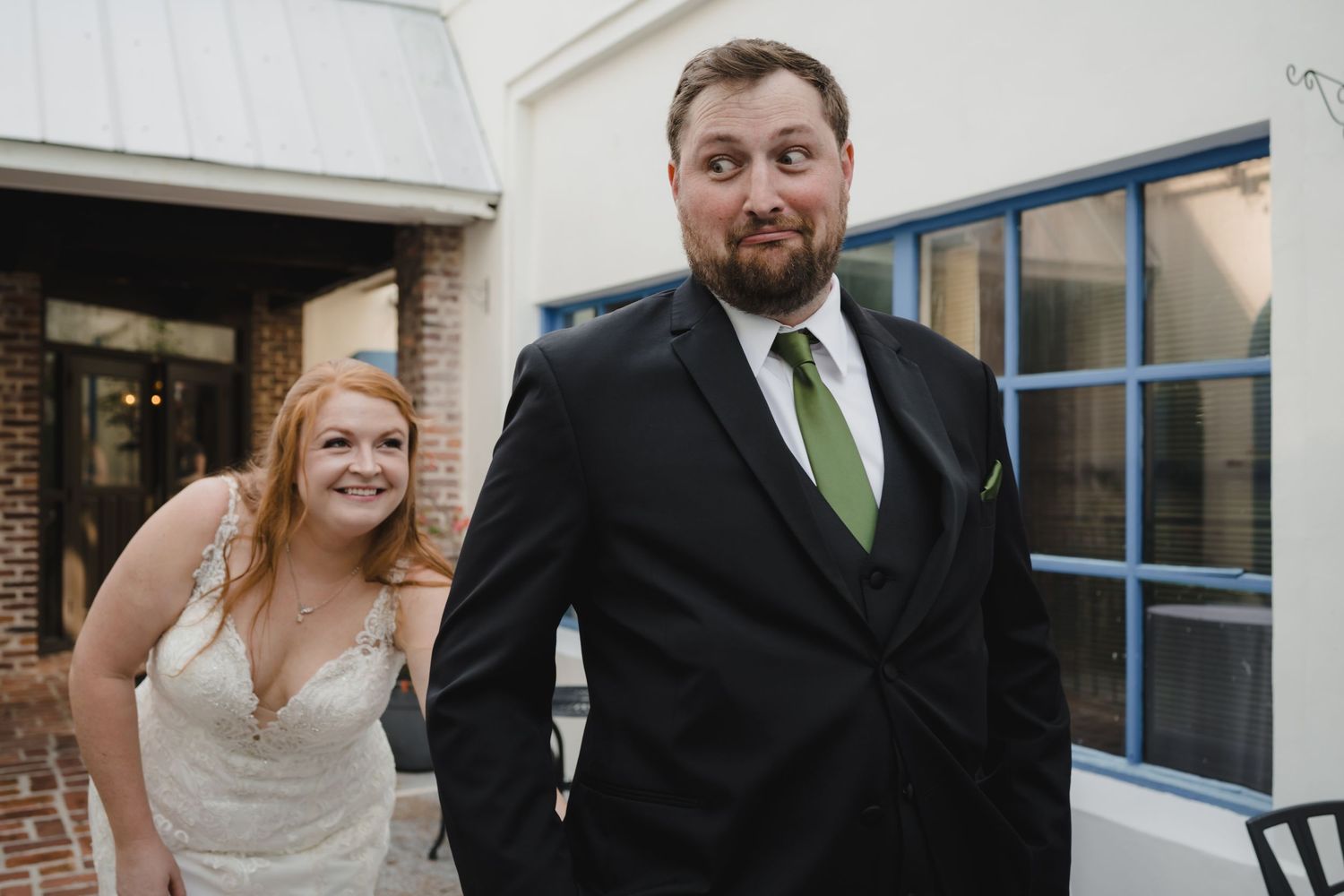 Smiling bride and bearded groom in black suit share a joyful first look moment outdoors.
