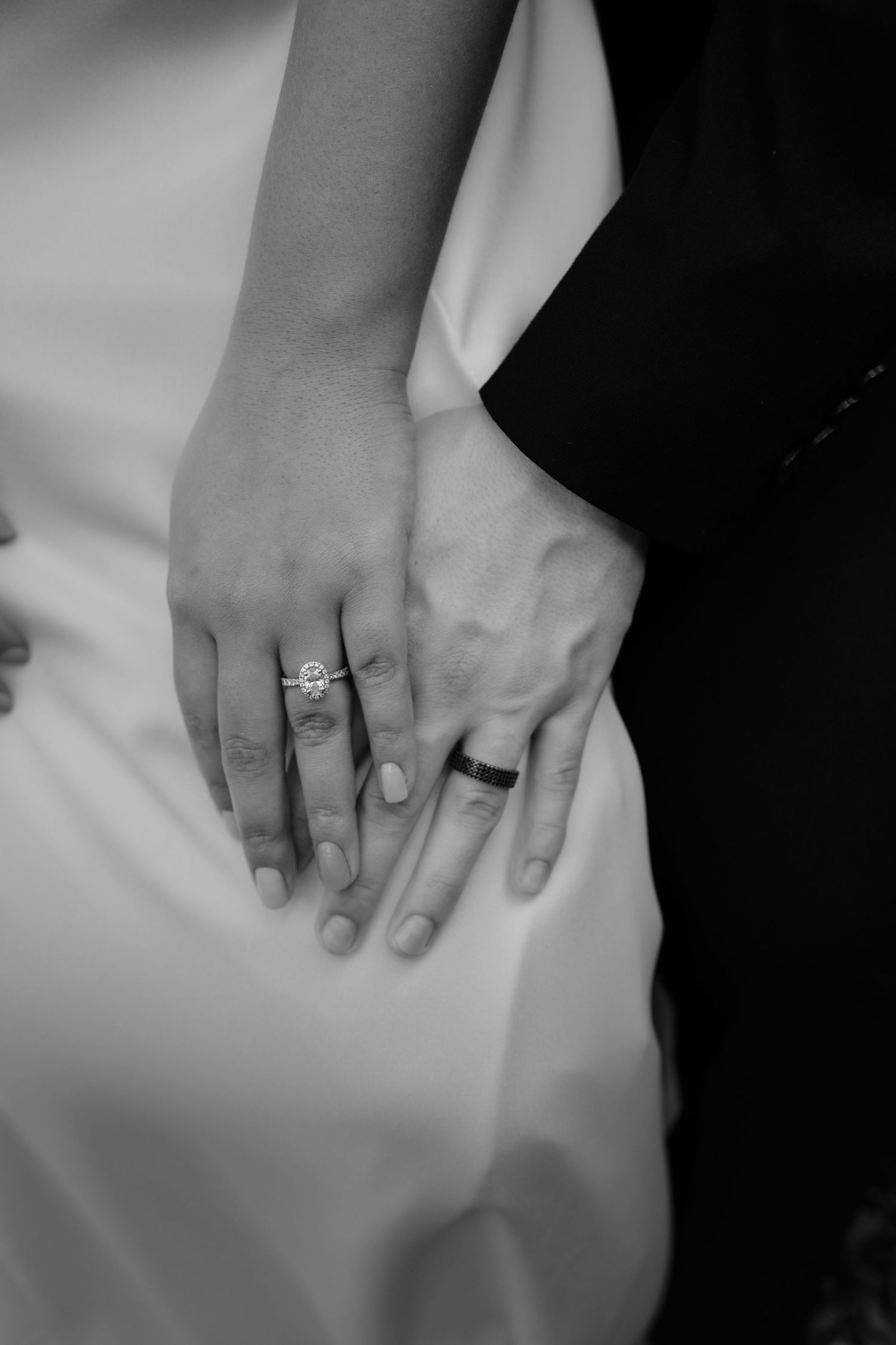 Black and white close-up of newlyweds hands showing diamond engagement ring and wedding bands.