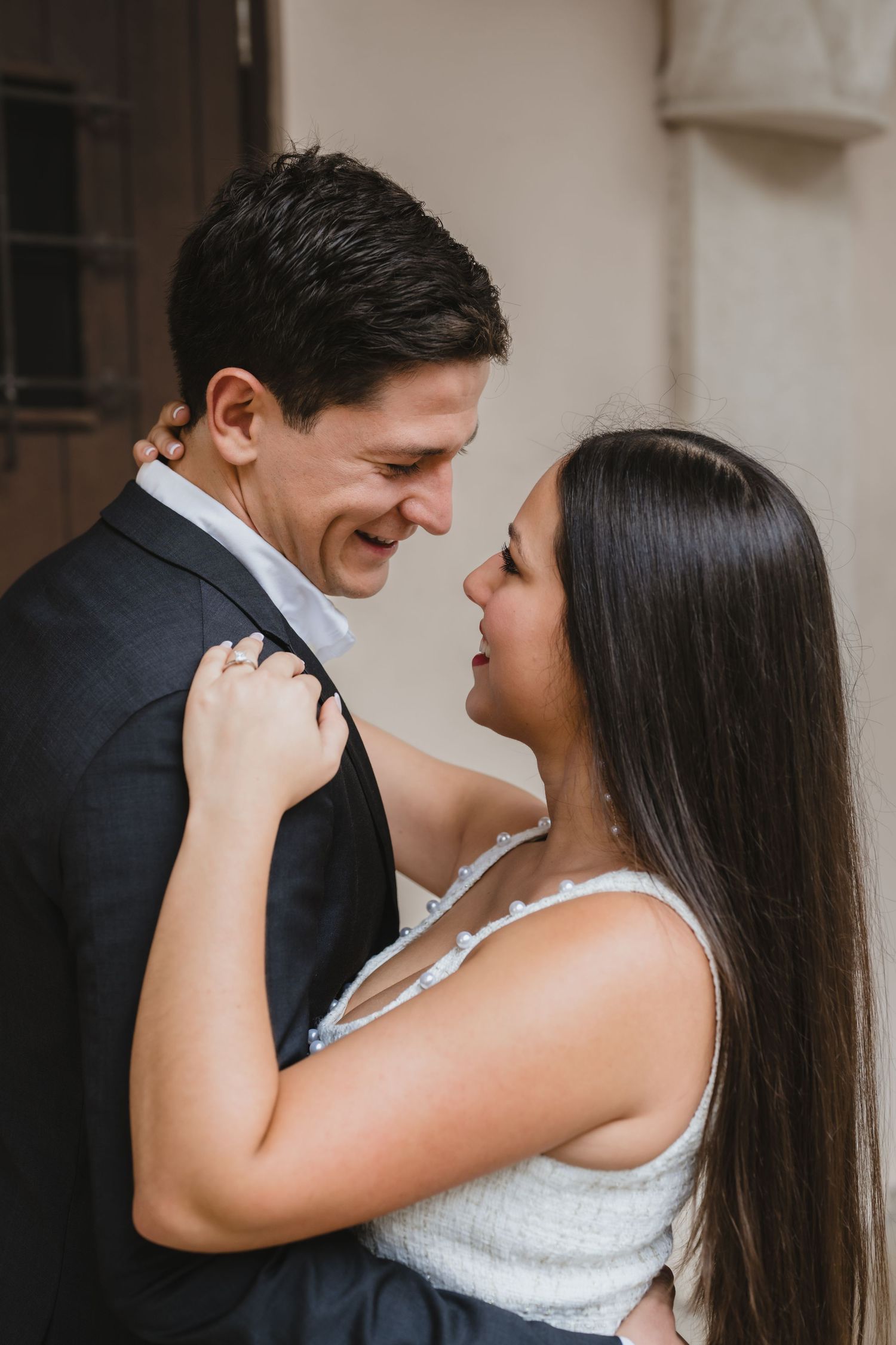 Smiling couple in a tender embrace during their engagement session against a warm neutral backdrop.