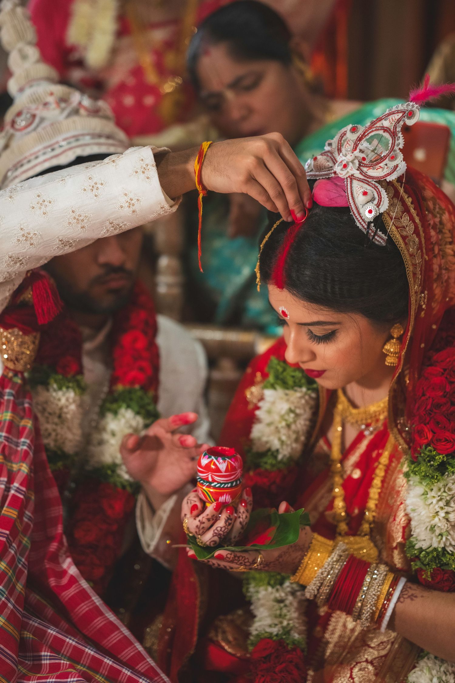 Indian groom applies sindoor to bride in red bridal attire during traditional Hindu wedding ceremony ritual.