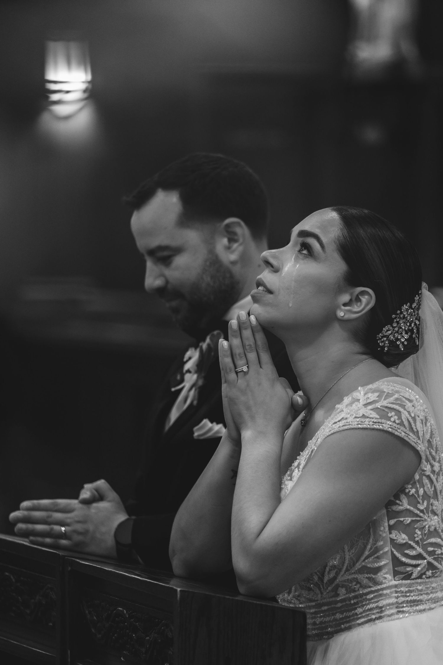 Bride prays with hands clasped beside groom during emotional church wedding ceremony.