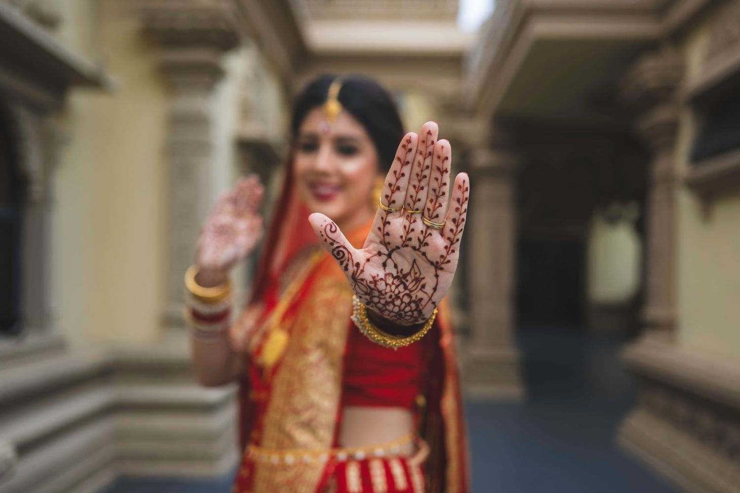 Indian bride in red lehenga smiles while showcasing intricate henna mehndi design on her palm.